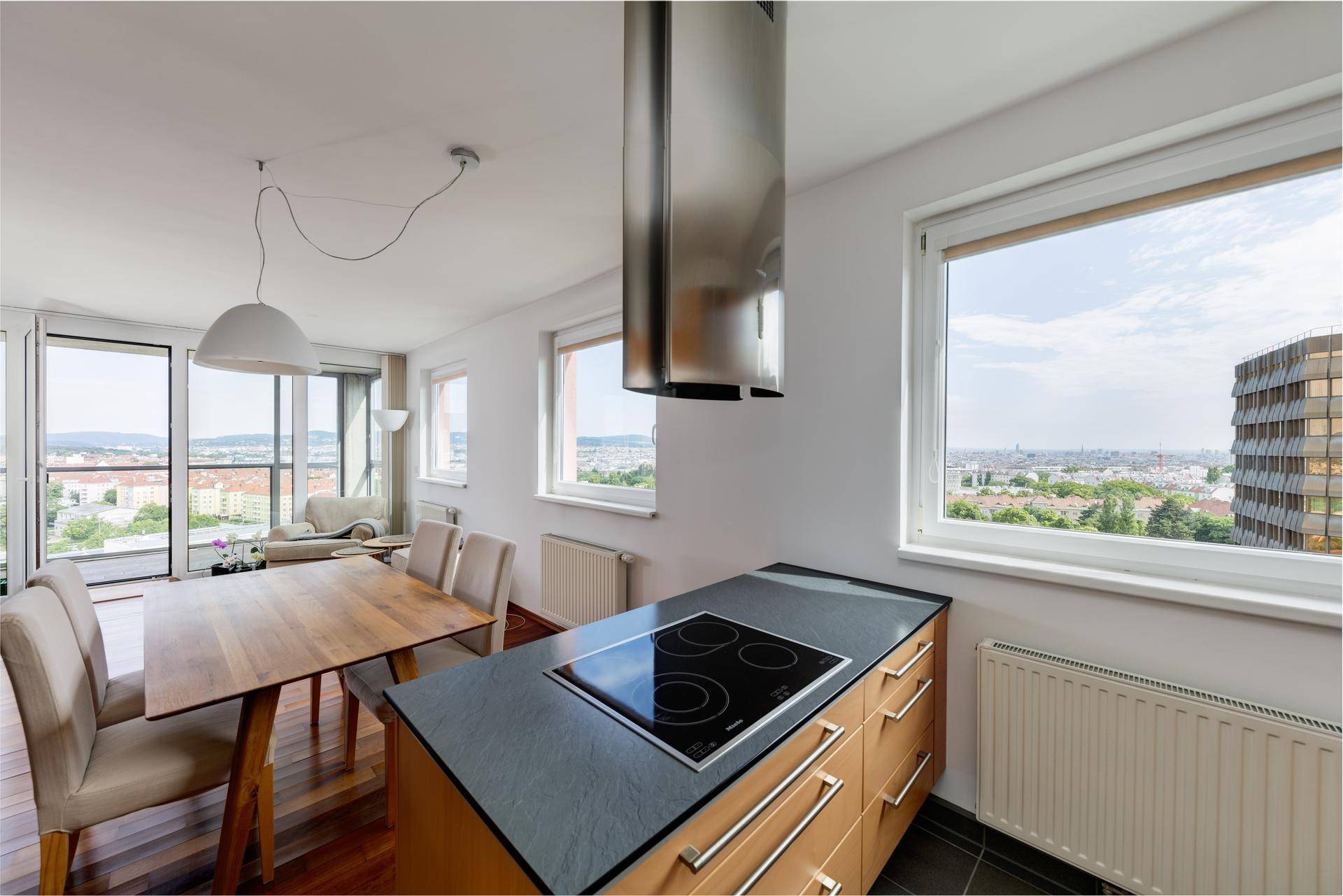 Moderne Küche mit Kochinsel, Induktionskochfeld und Essbereich mit Stadtblick.