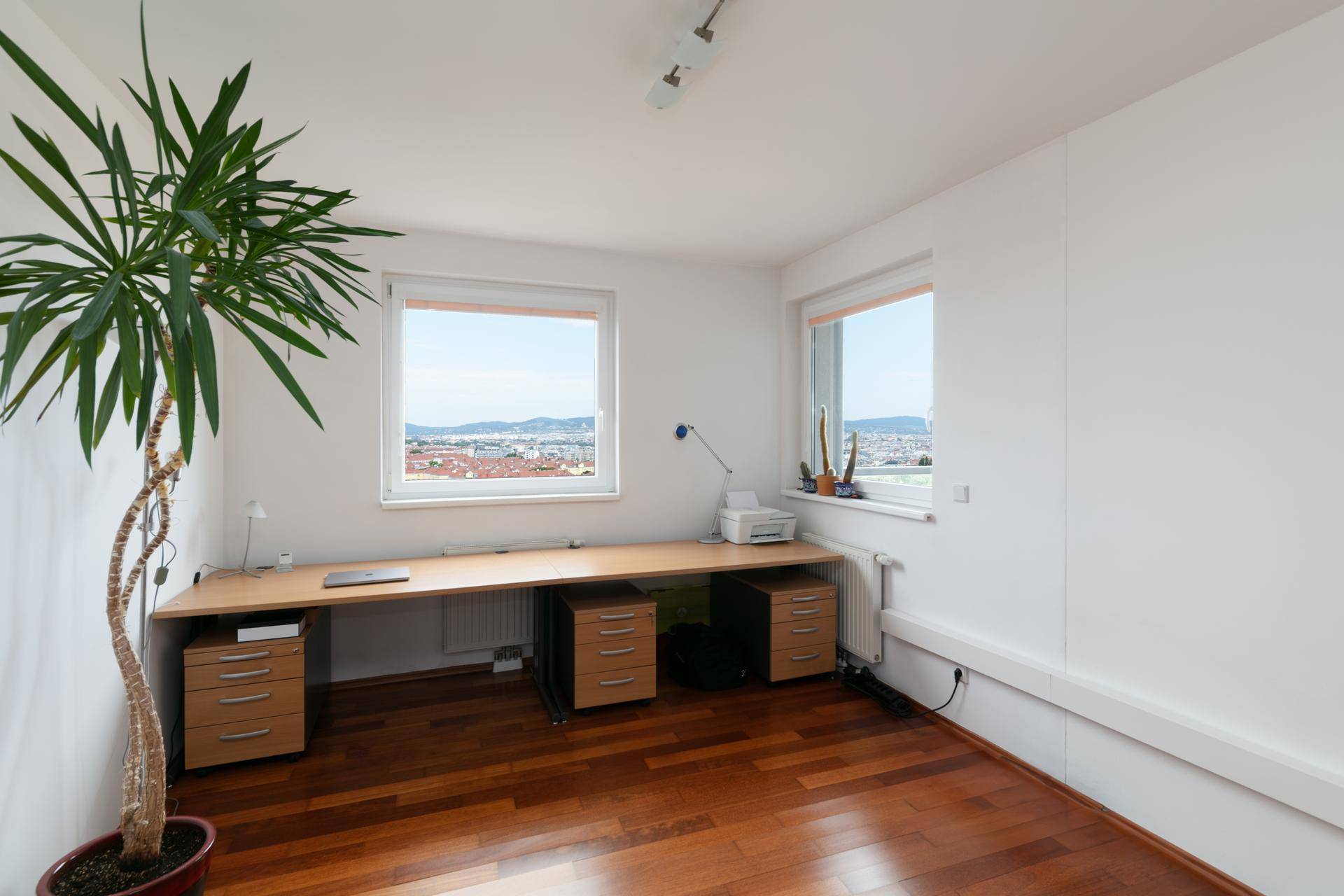 Helles Büro mit Holzparkettboden, großem Schreibtisch und Fenstern mit Weitblick.