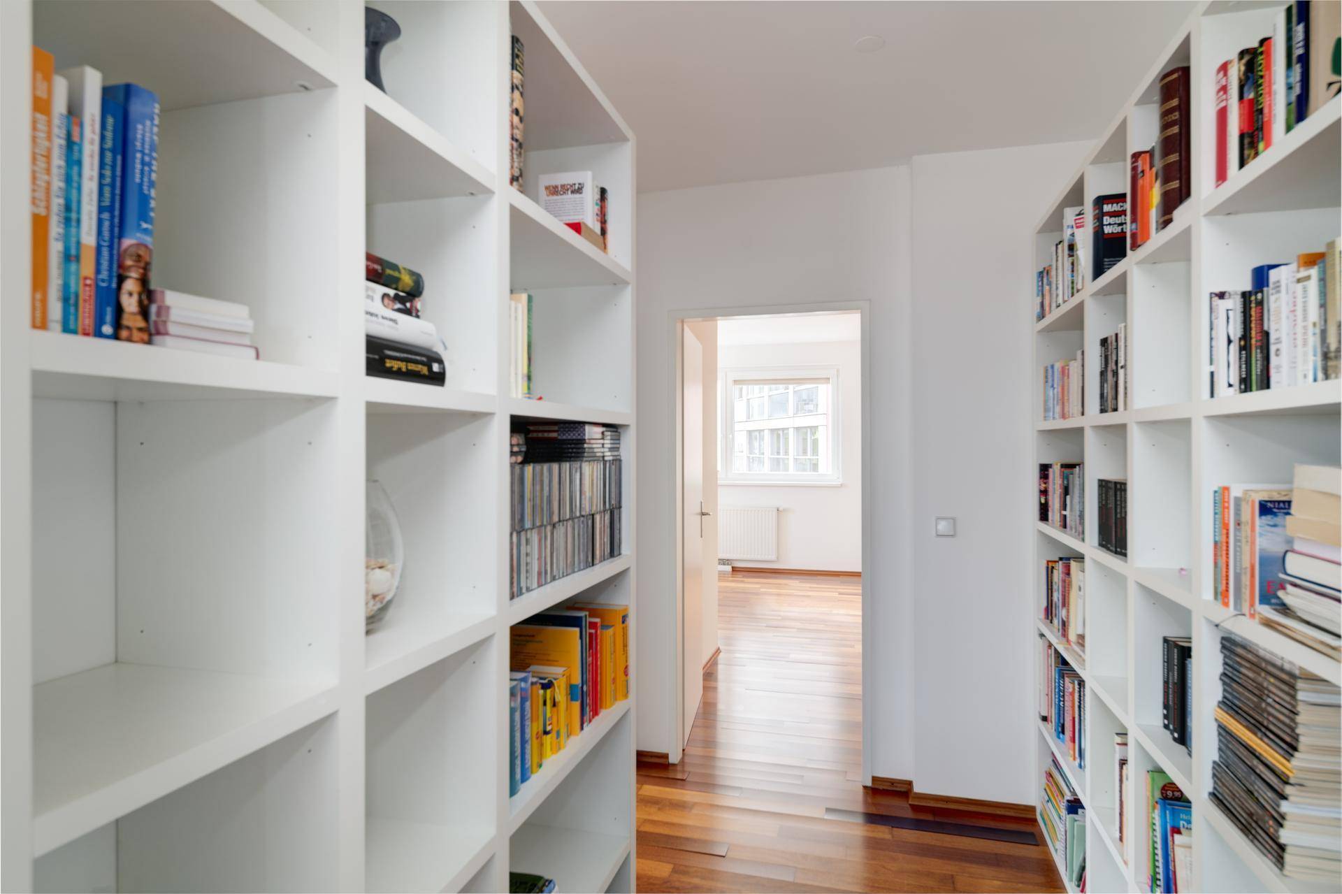 Heller Flur mit Holzparkettboden und integrierten Bücherregalen an beiden Seiten.
