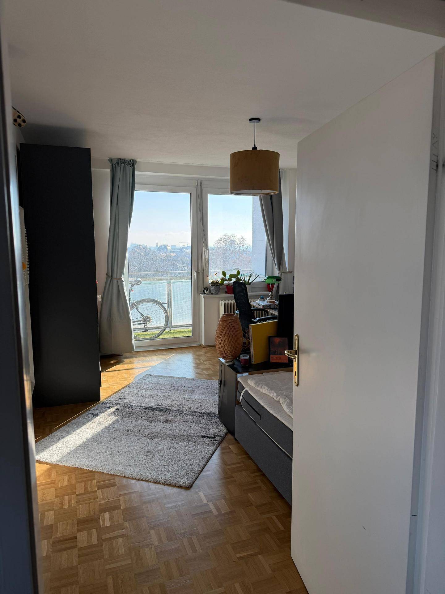 Helles Wohnzimmer mit großen Fenstern, Parkettboden und direktem Zugang zum Balkon.