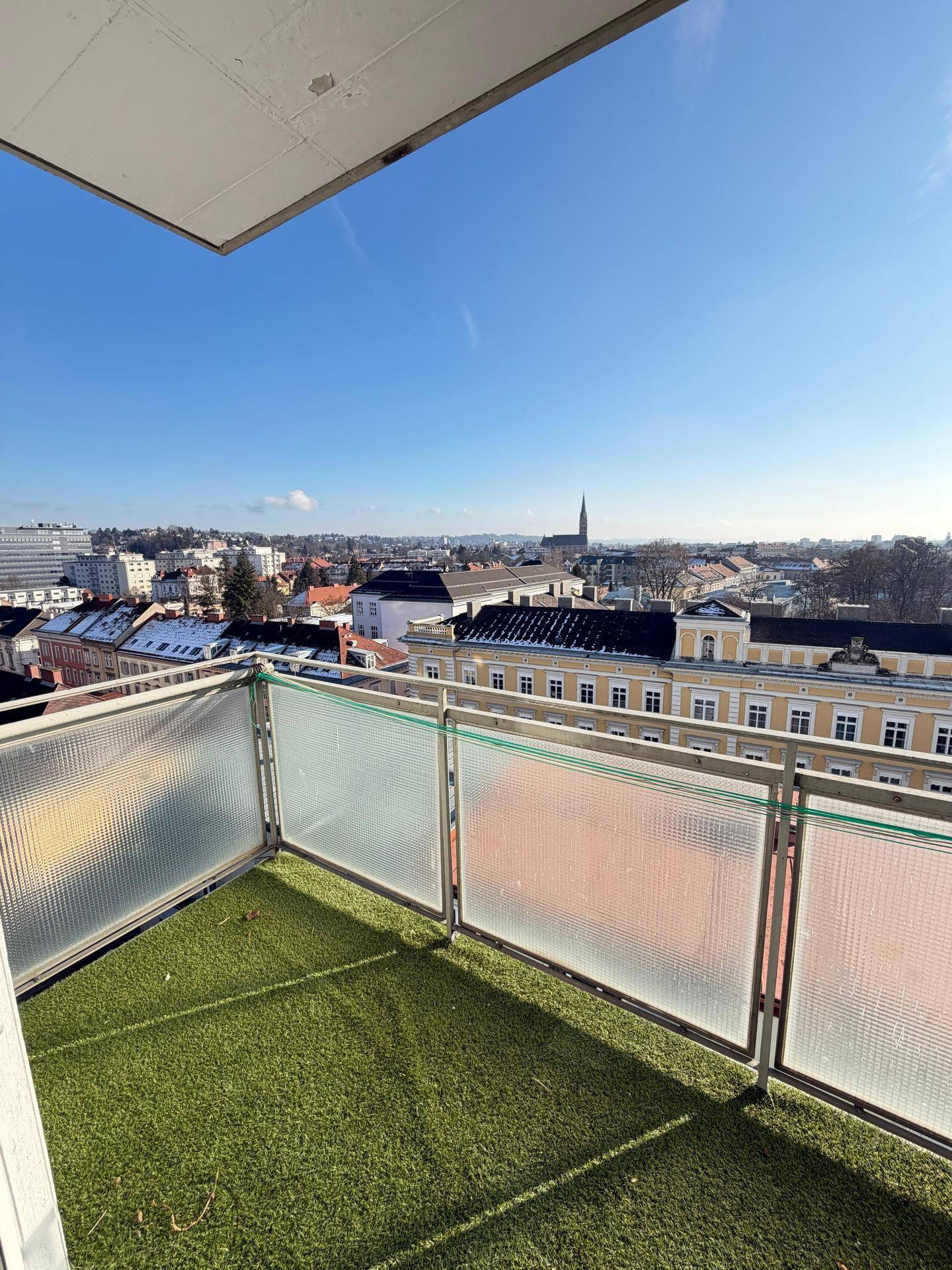 Sonniger Balkon mit Kunstrasen und weitem Panoramablick über die Stadt.