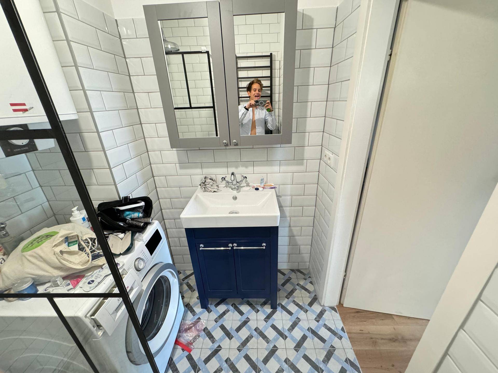 Modernes Badezimmer mit Waschbecken, Spiegelschrank, Waschmaschine und Fliesenboden.