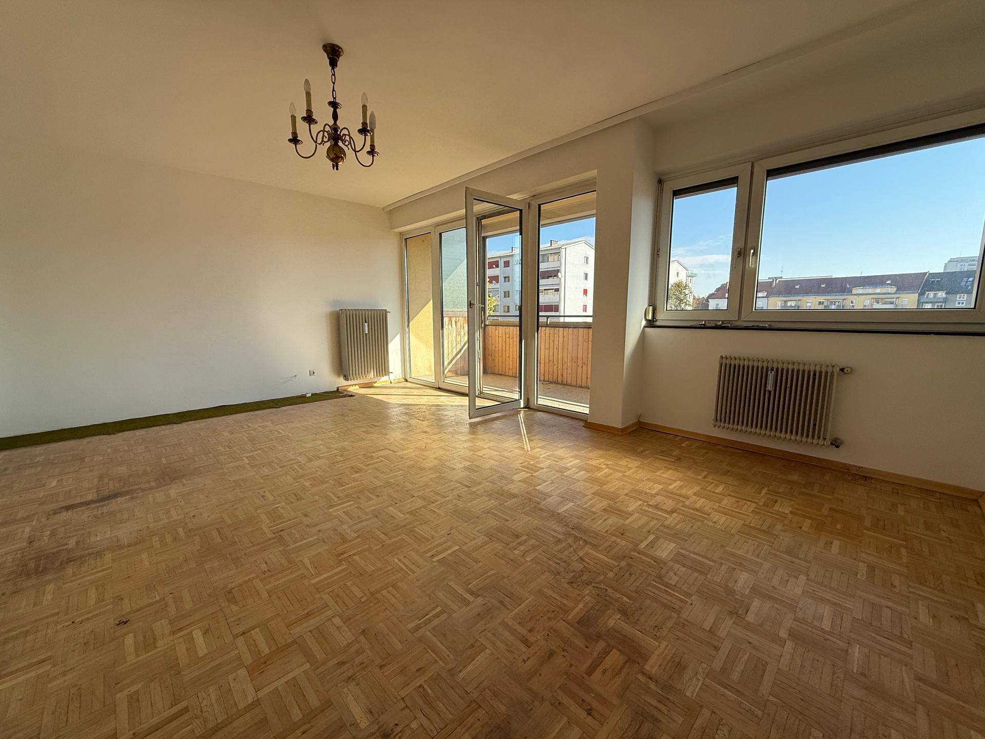 Geräumiges Wohnzimmer mit Parkettboden und Zugang zu einem sonnigen Balkon.