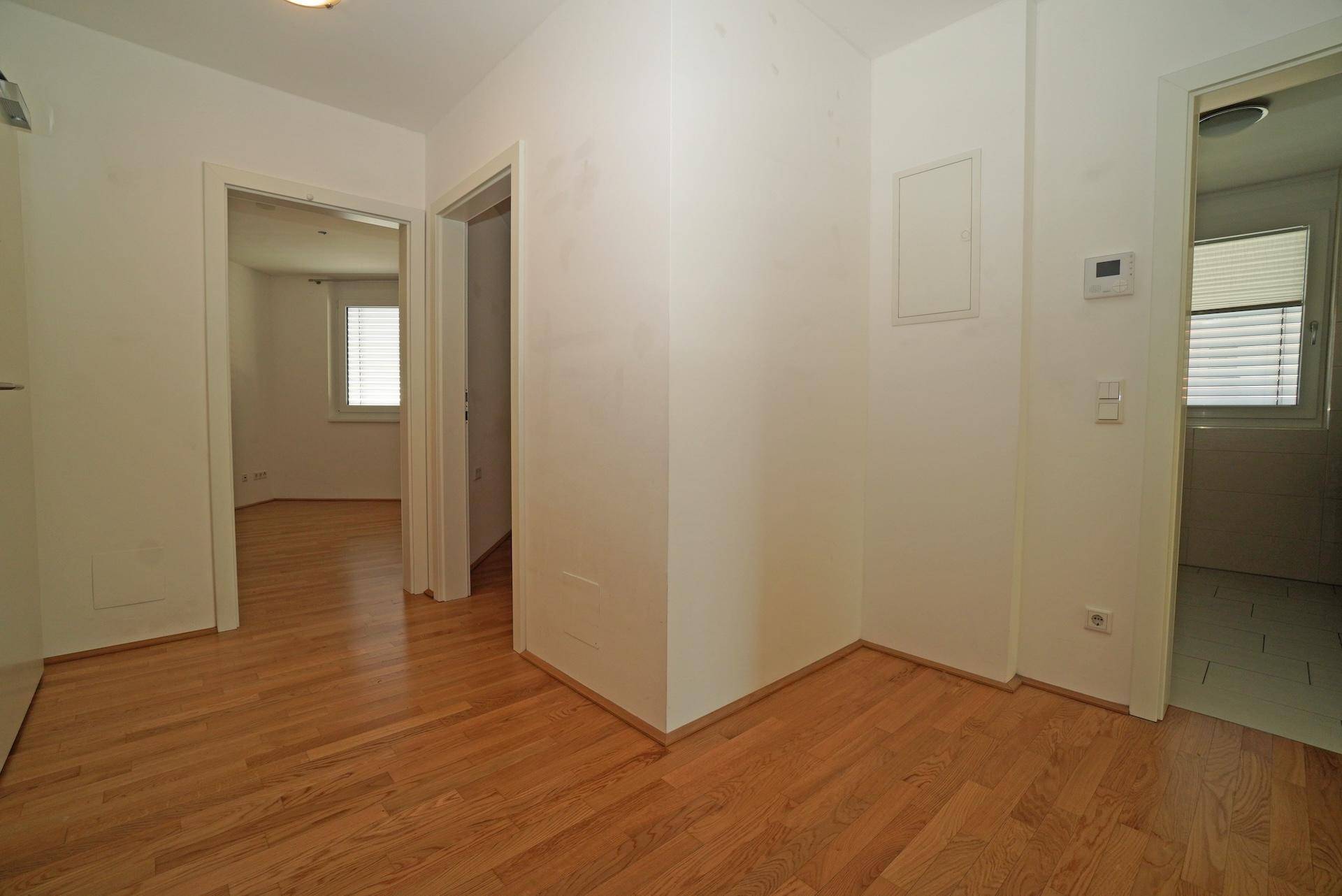 Heller Flur mit Holzboden und weißen Wänden, der Zugang zu verschiedenen Räumen der Wohnung bietet.