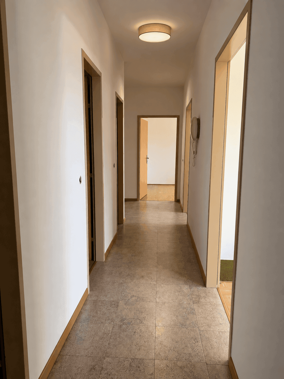 Langer Flur mit Fliesenboden und Türen zu verschiedenen Räumen.