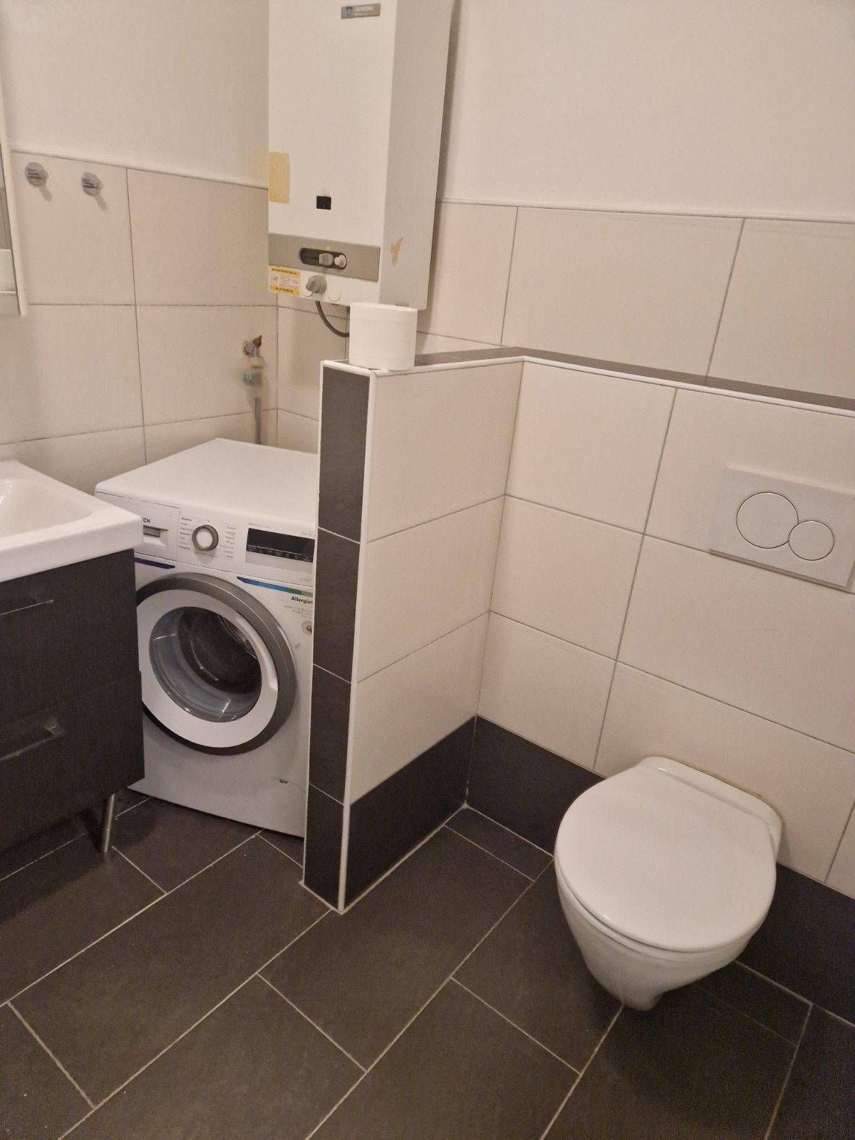 Modern gefliestes Badezimmer mit Toilette, Waschbecken und Anschluss für eine Waschmaschine.
