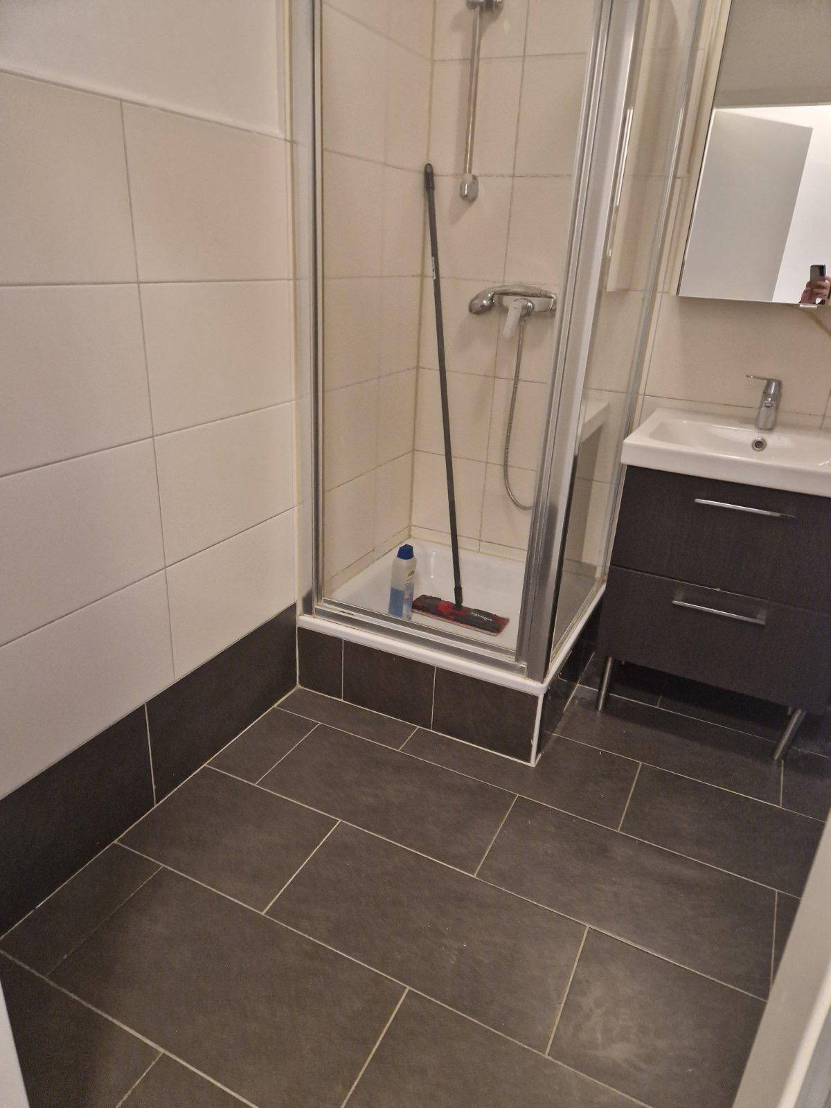 Badezimmer mit Duschkabine, Waschbeckenunterschrank und dunklen Bodenfliesen.