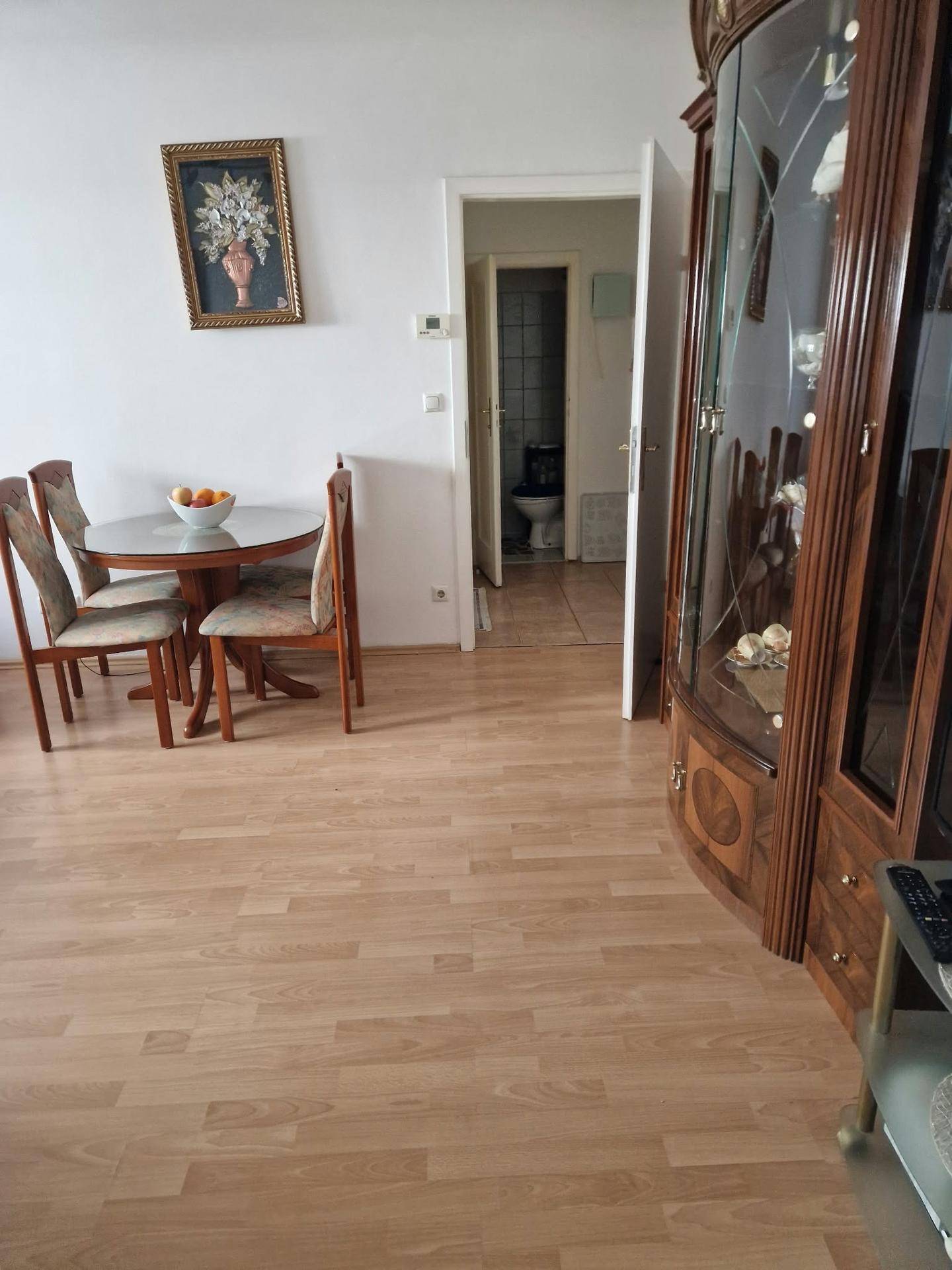 Essbereich mit rundem Glastisch und Stühlen, einer Vitrine und einem Durchgang zu einem Badezimmer.
