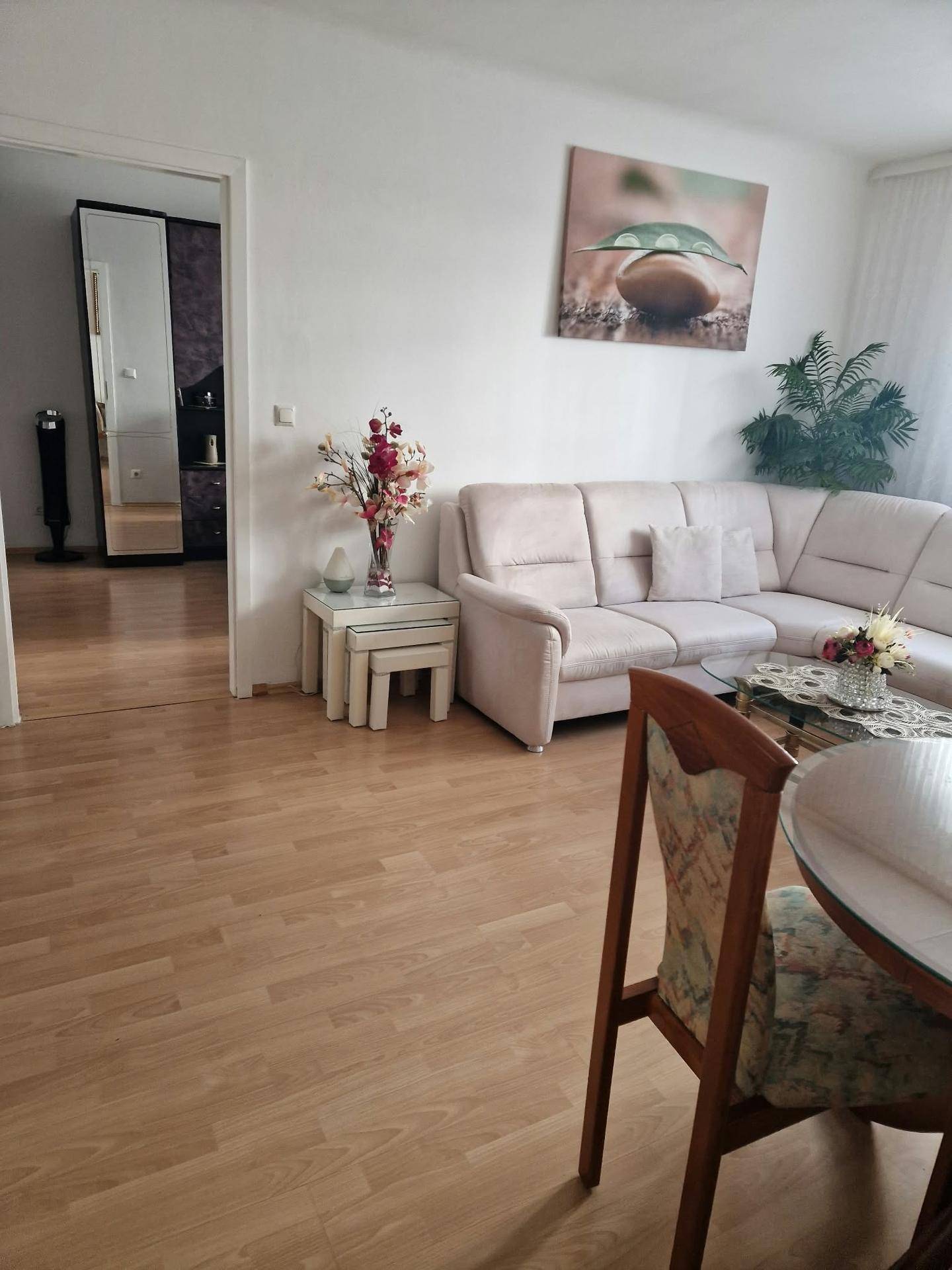 Gemütlicher Wohnbereich mit einem hellen Ecksofa, Beistelltischen und einem Blick in einen angrenzenden Raum.