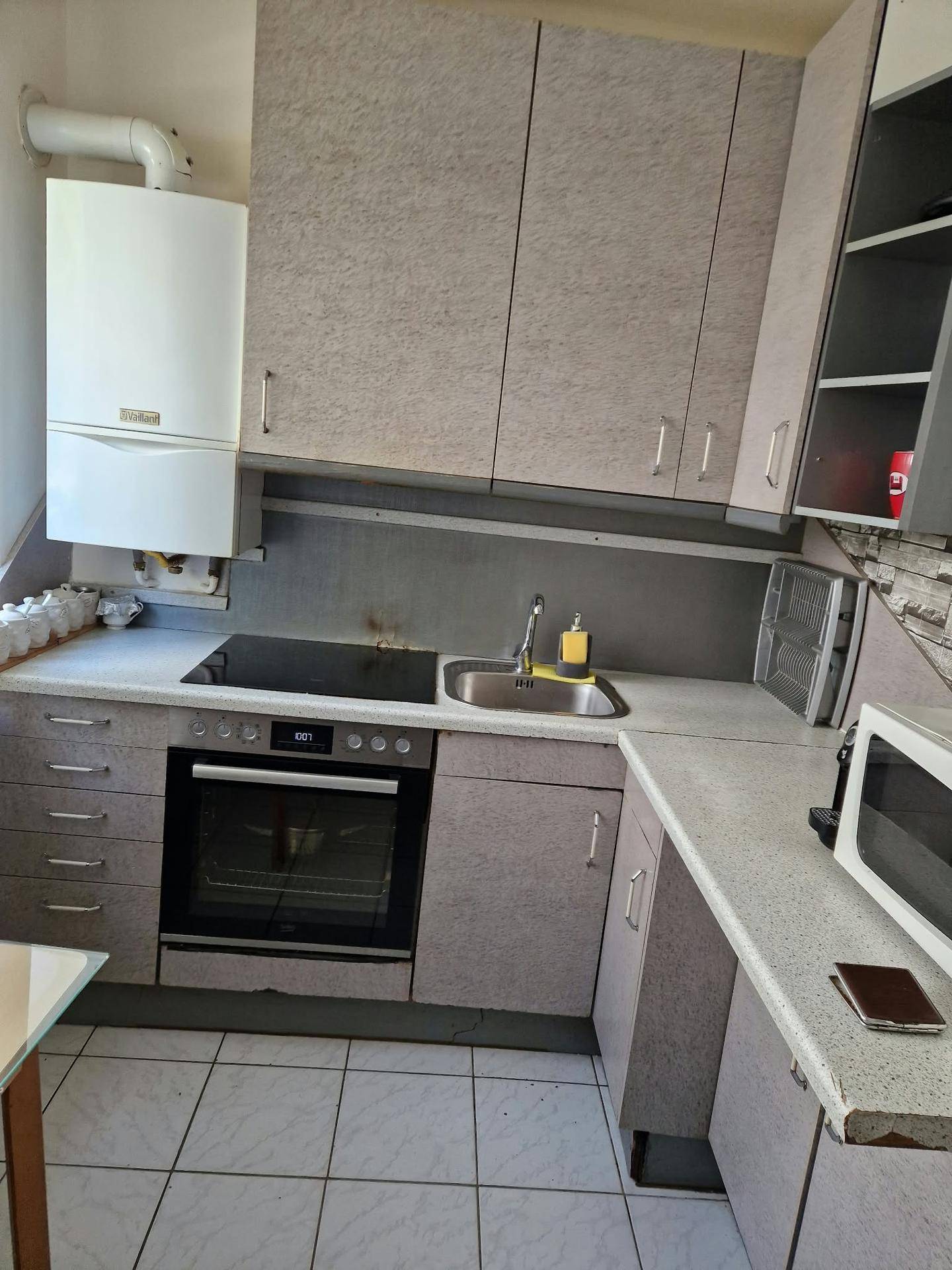 Funktionale Küche mit grauen Schränken, Spüle, Backofen und einem an der Wand montierten Heizkessel.