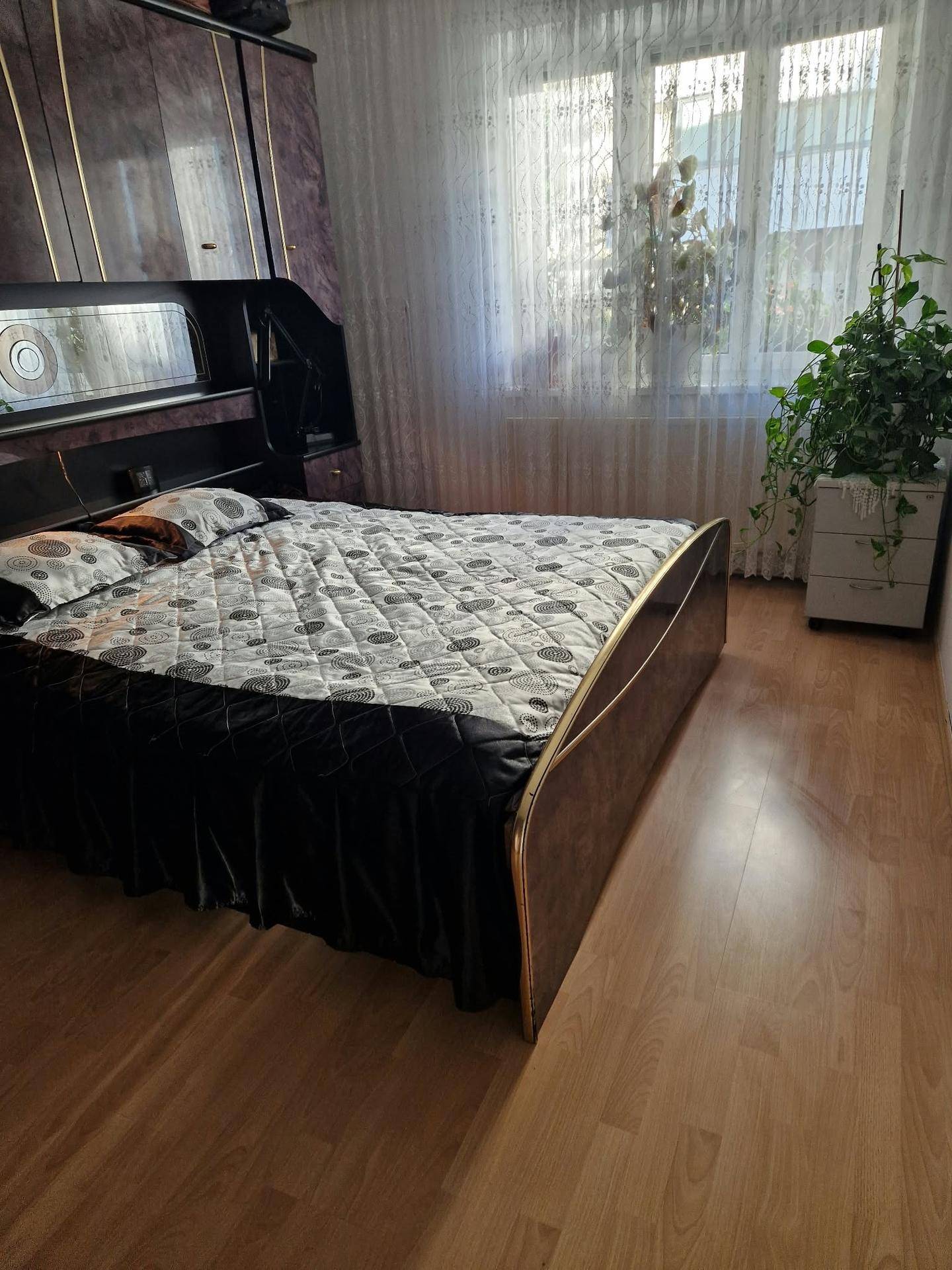 Schlafzimmer mit einem bequemen Bett, gemusterten Bettwaren und einem großen Fenster, das viel Licht hereinlässt.