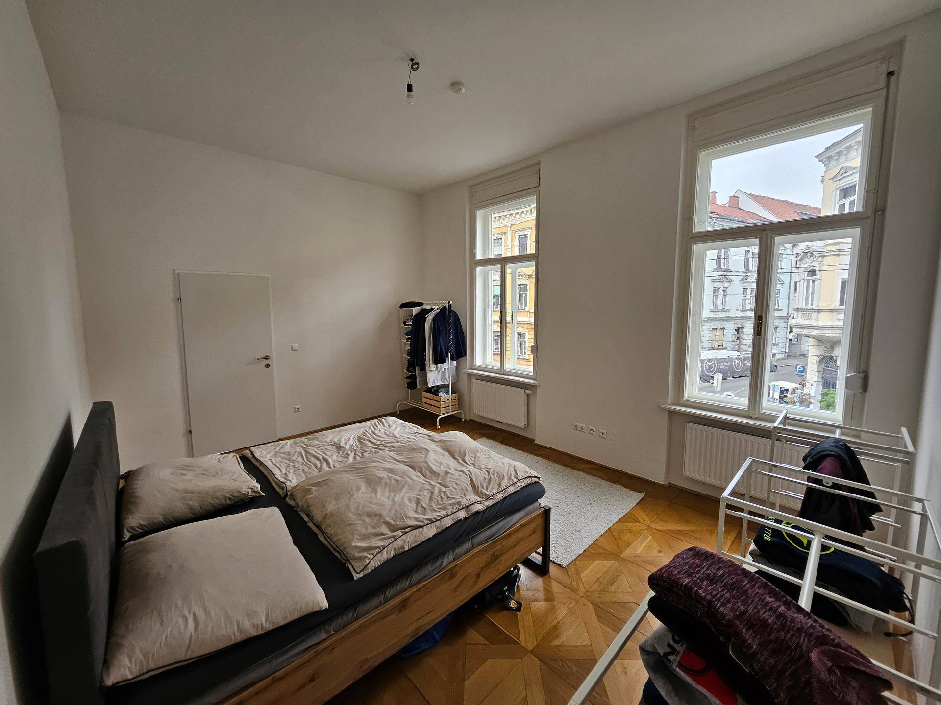 Geräumiges Schlafzimmer mit zwei Fenstern, Holzbett und praktischer Kleideraufbewahrung.
