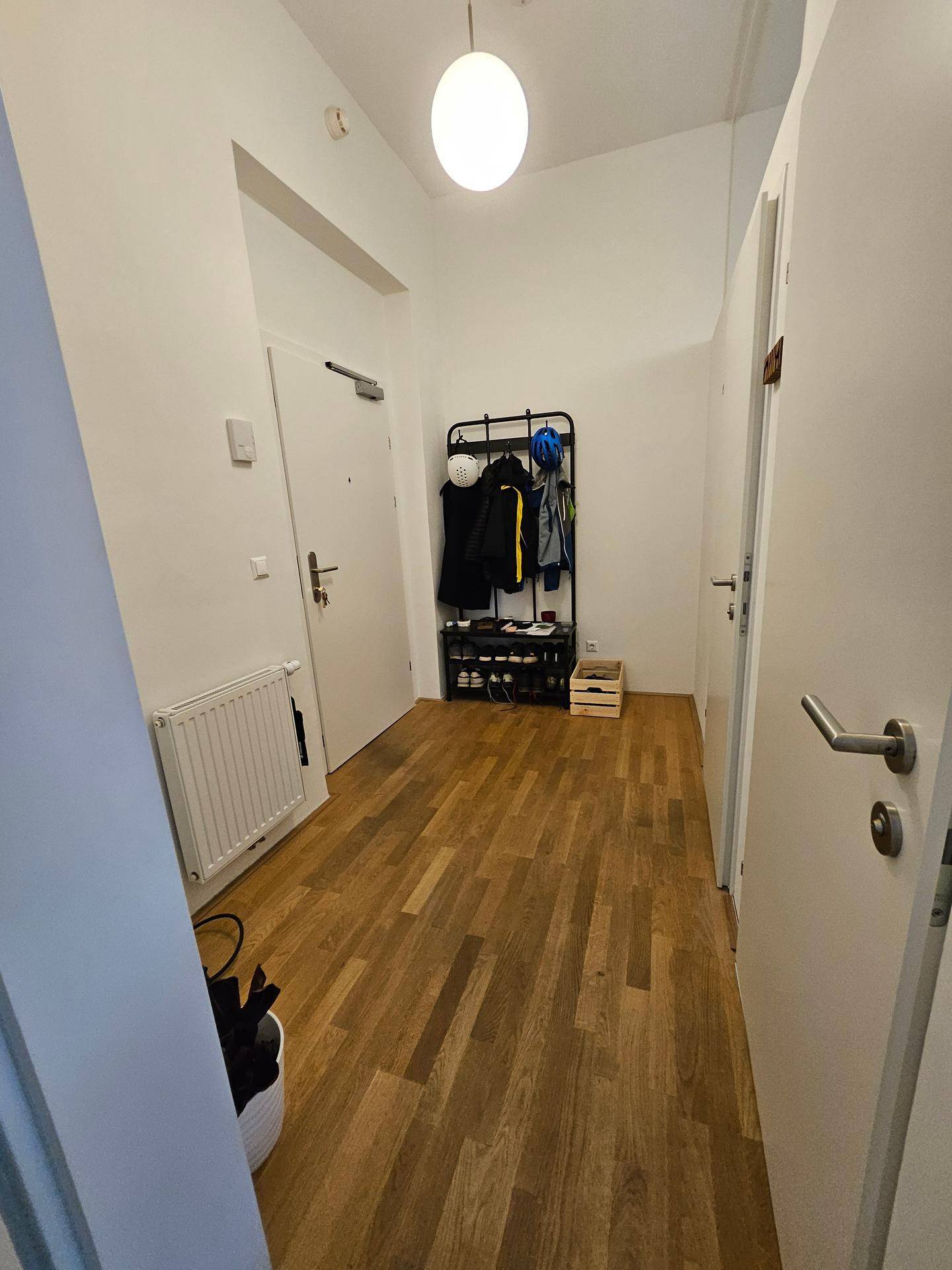 Heller Flur mit Holzfußboden, Garderobe und Heizkörper.