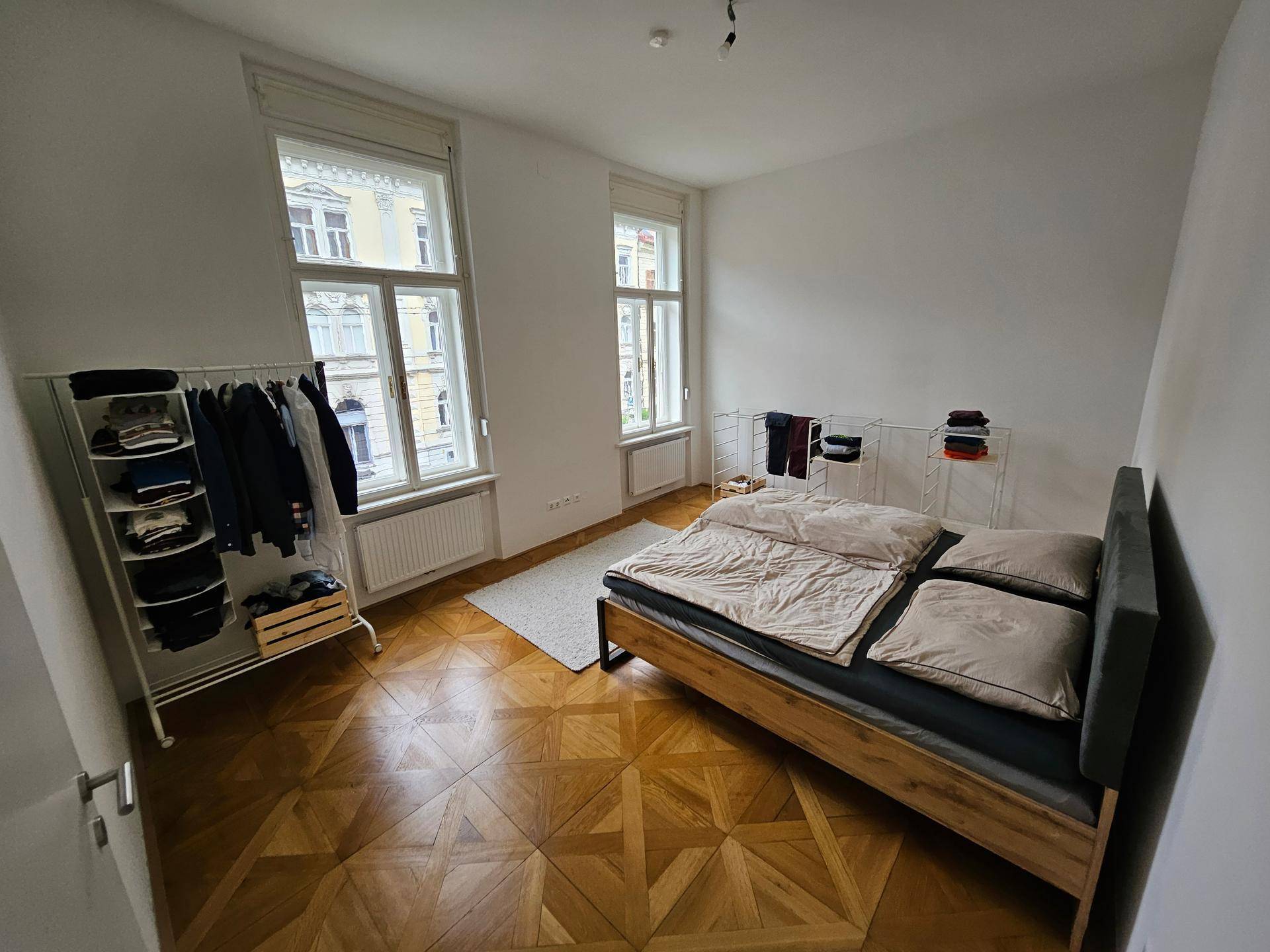 Schlafzimmer mit Parkettboden, viel Tageslicht und minimalistischer Einrichtung.