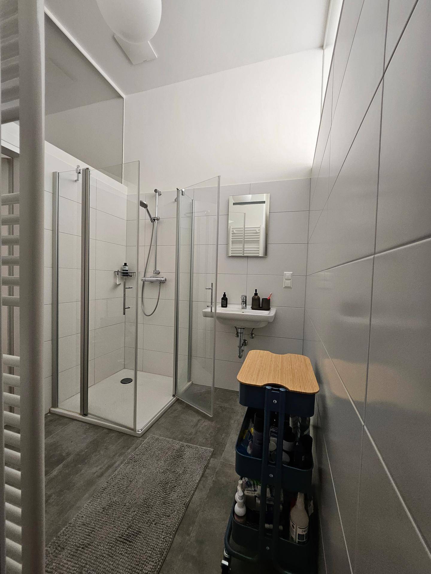 Modernes Badezimmer mit begehbarer Dusche, grauen Bodenfliesen und weißer Wandverkleidung.