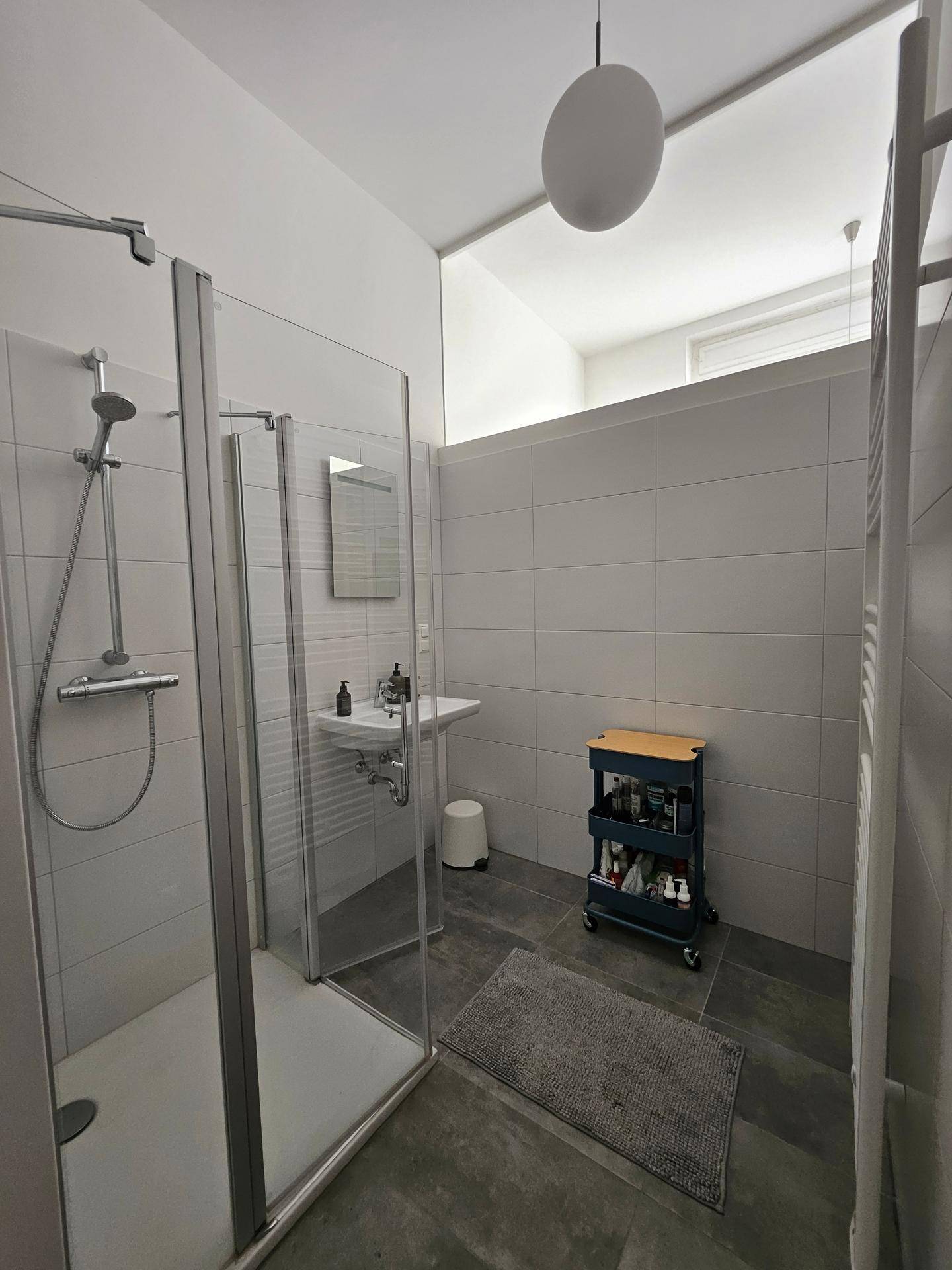 Helles Badezimmer mit moderner Duschkabine, Einzelwaschbecken und Handtuchheizkörper.