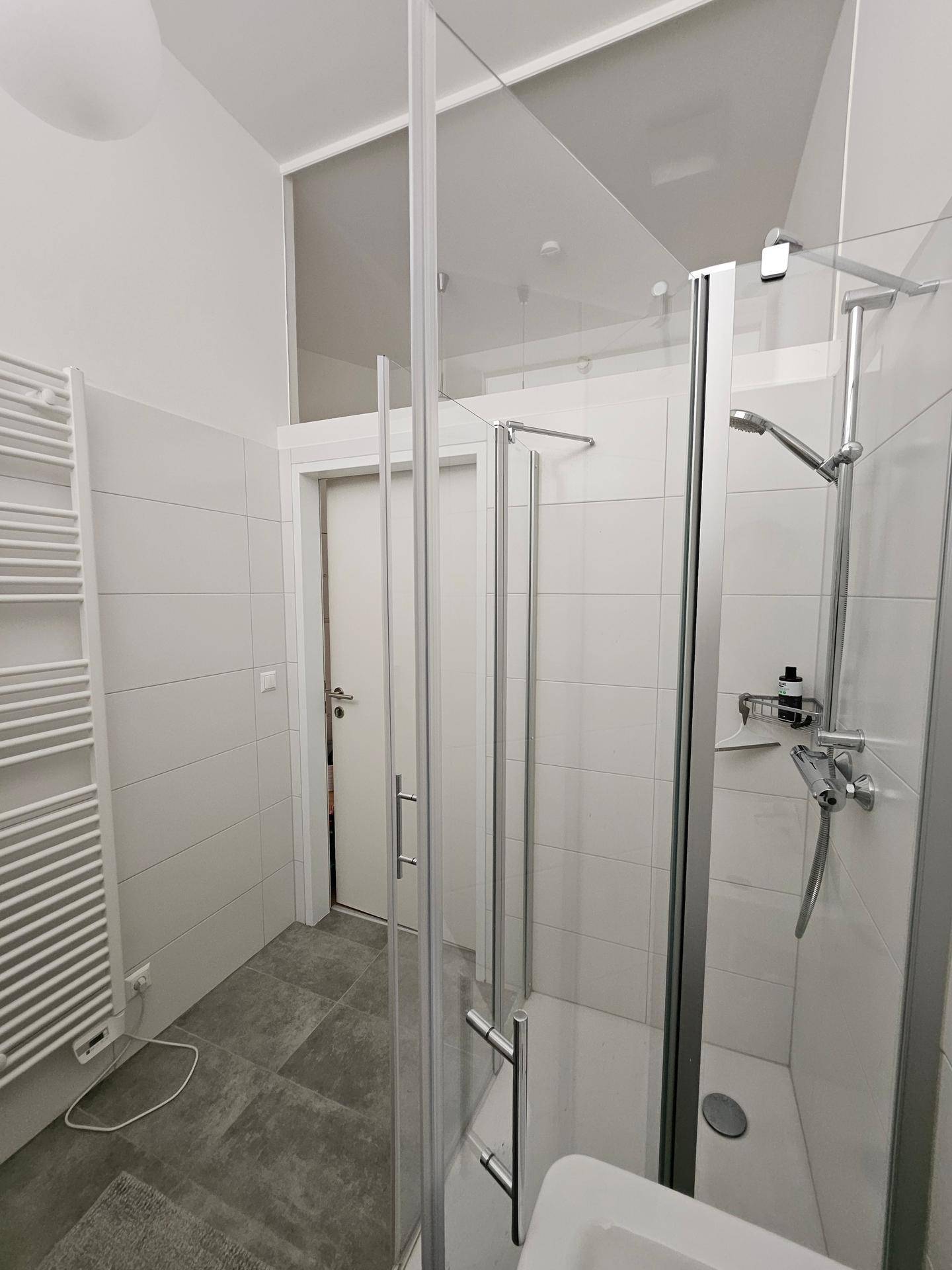 Badezimmer mit begehbarer Dusche, modernen Fliesen und Zugang zu einem weiteren Raum.