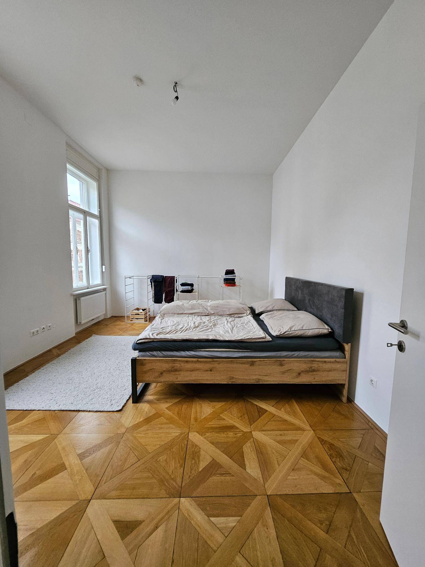 Helles Schlafzimmer mit Doppelbett, elegantem Parkettboden und großem Fenster.