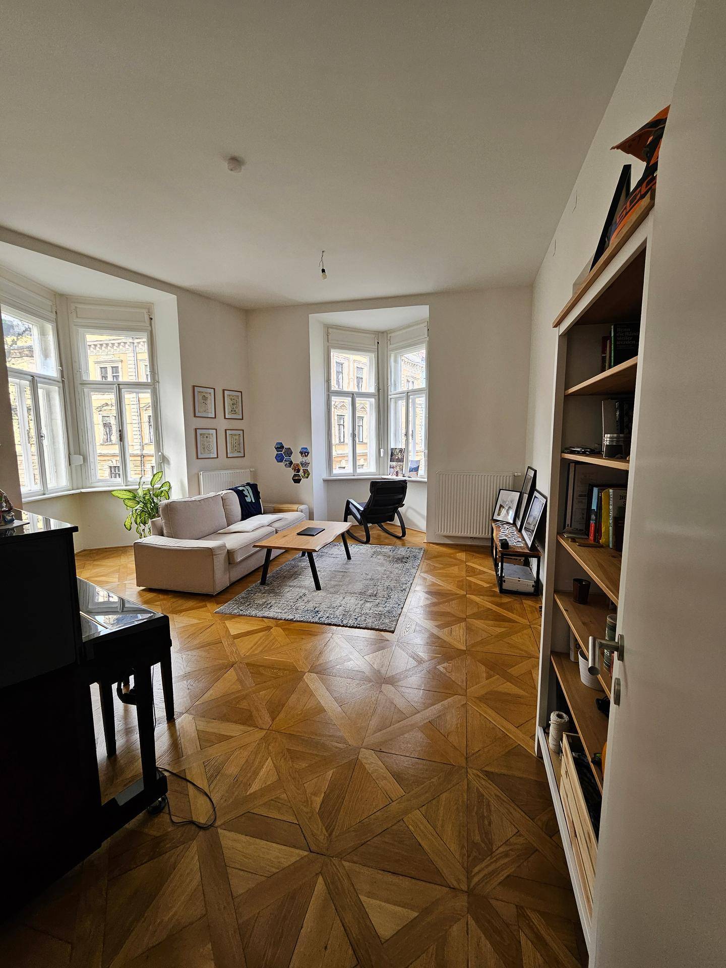 Gemütliches Wohnzimmer mit Parkettboden, Erkerfenstern und einem Bücherregal.
