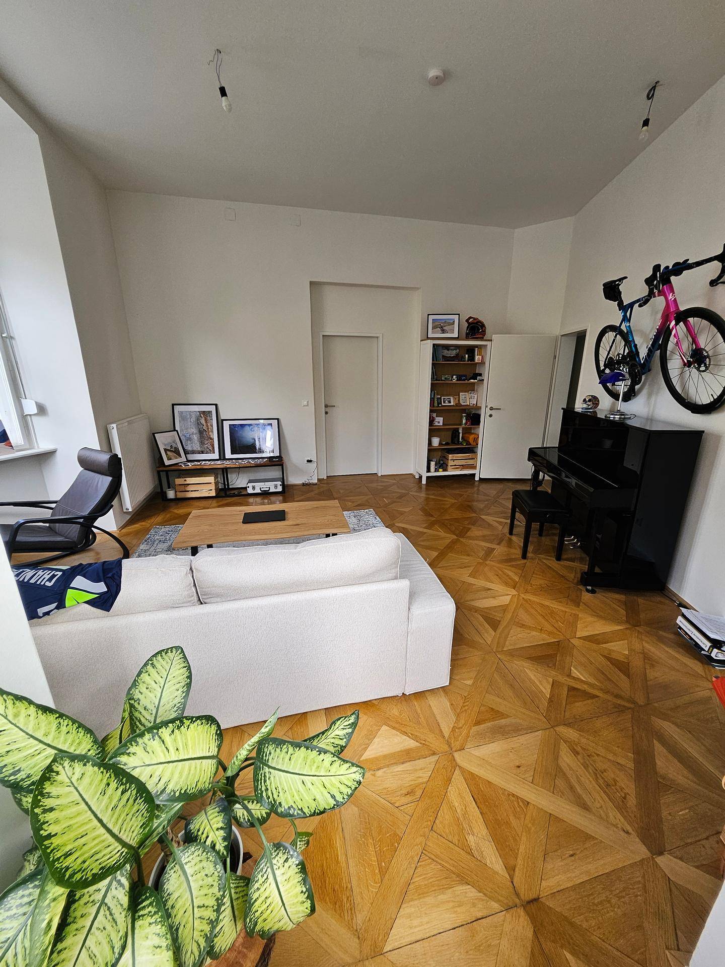 Helles Wohnzimmer mit Parkettboden, bequemer Couch und einem dekorativen Klavier.