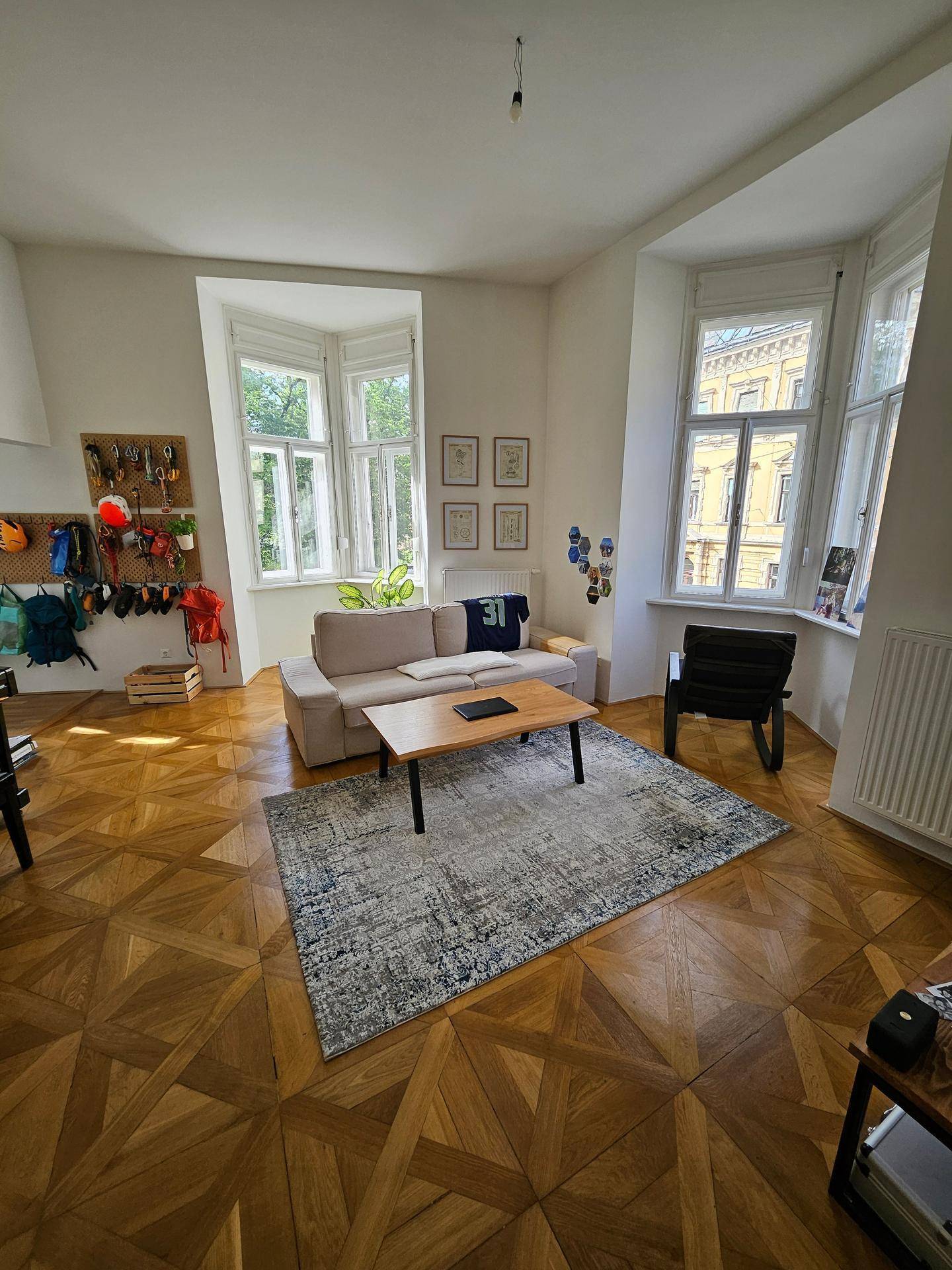 Geräumiges Wohnzimmer mit hellem Parkett, zwei Erkerfenstern und funktionaler Wandorganisation.