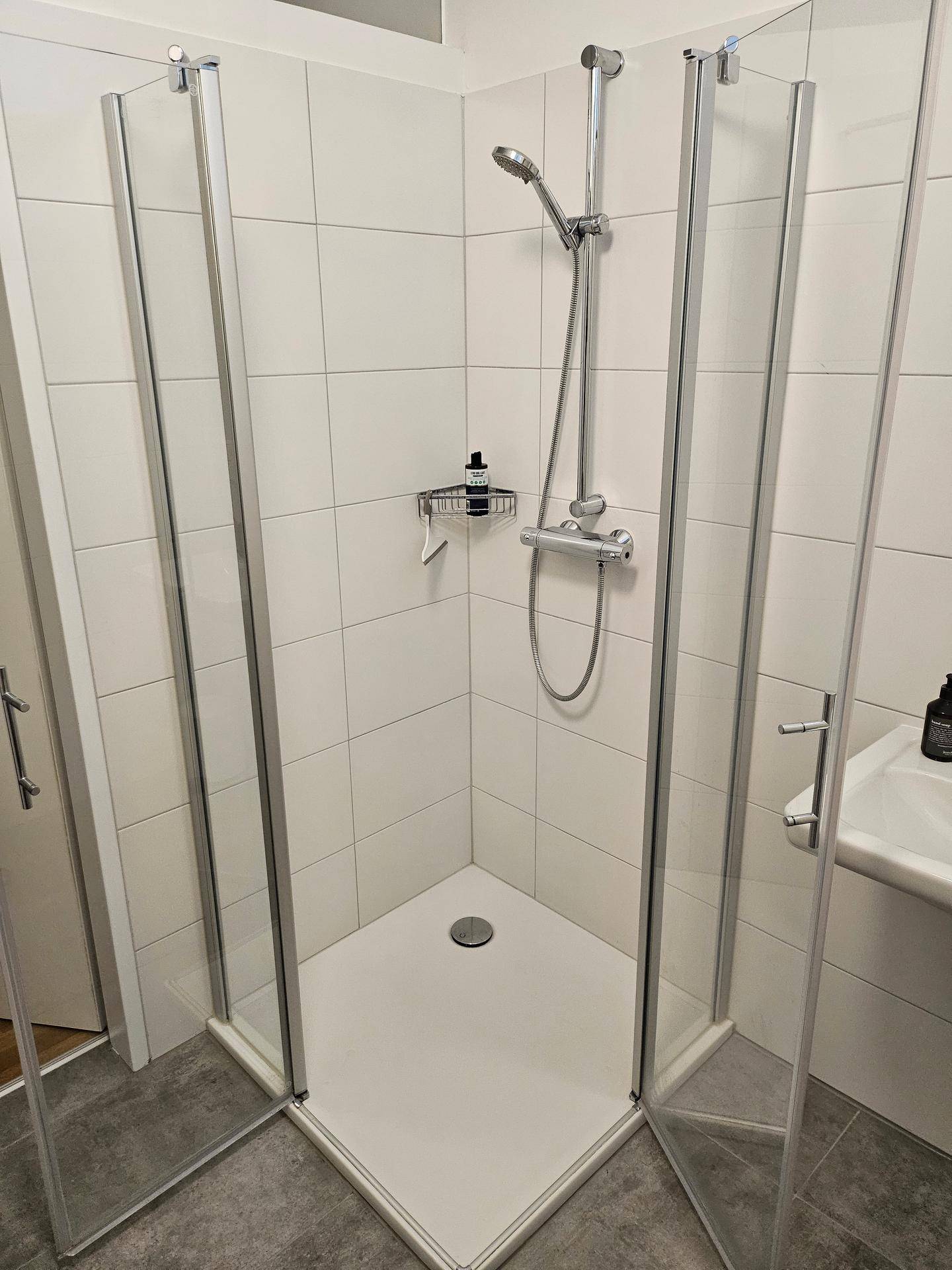 Moderne Eckdusche mit Glaswänden und weißen Fliesen im Badezimmer.