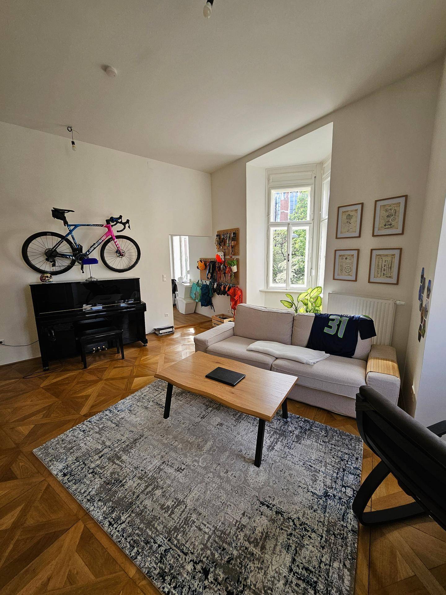 Wohnzimmer mit Parkettboden, Klavier und einem an der Wand montierten Fahrrad als Dekoration.