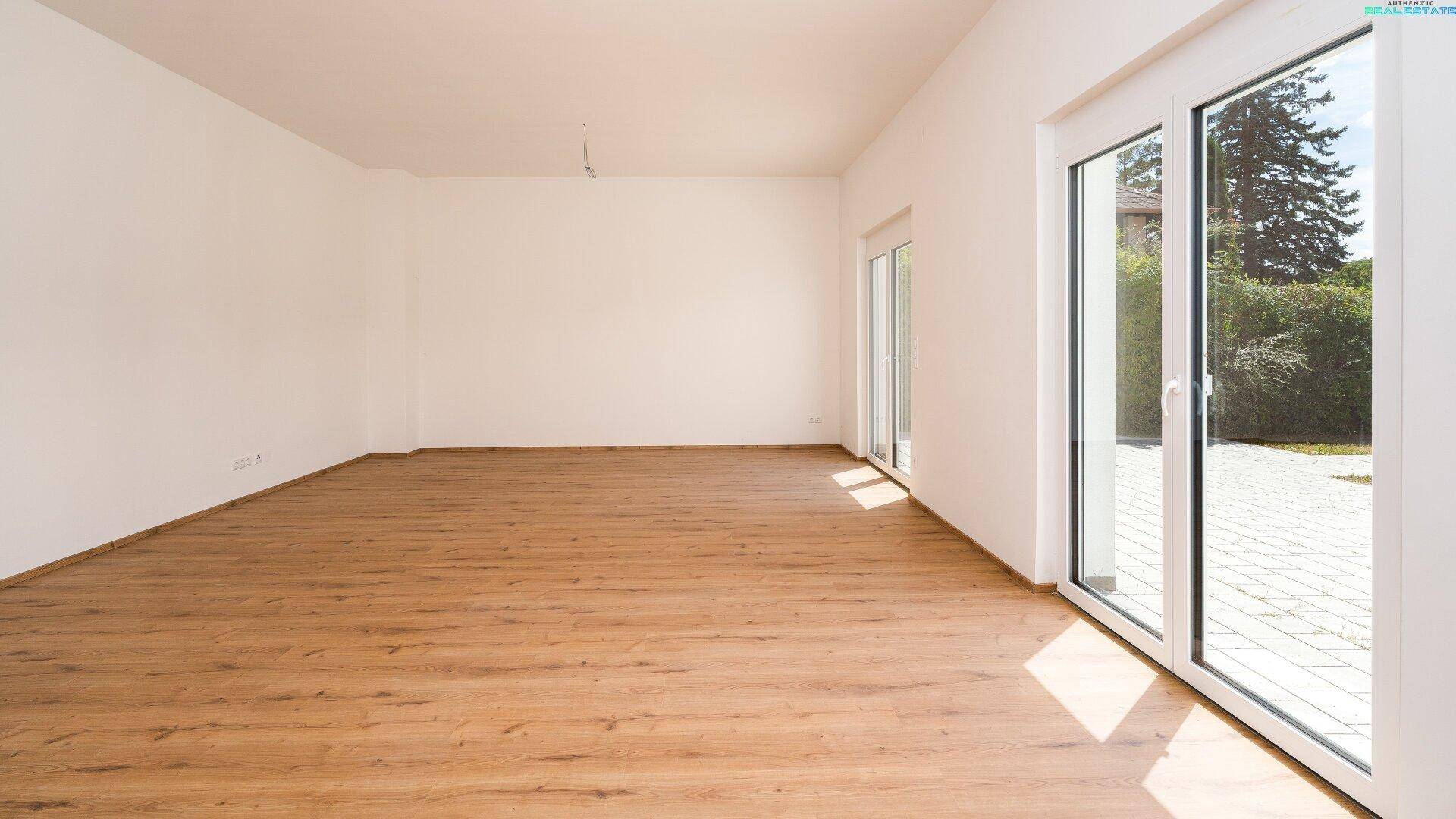 Heller, leerer Wohnraum mit Laminatboden und großen Schiebetüren zum Außenbereich.