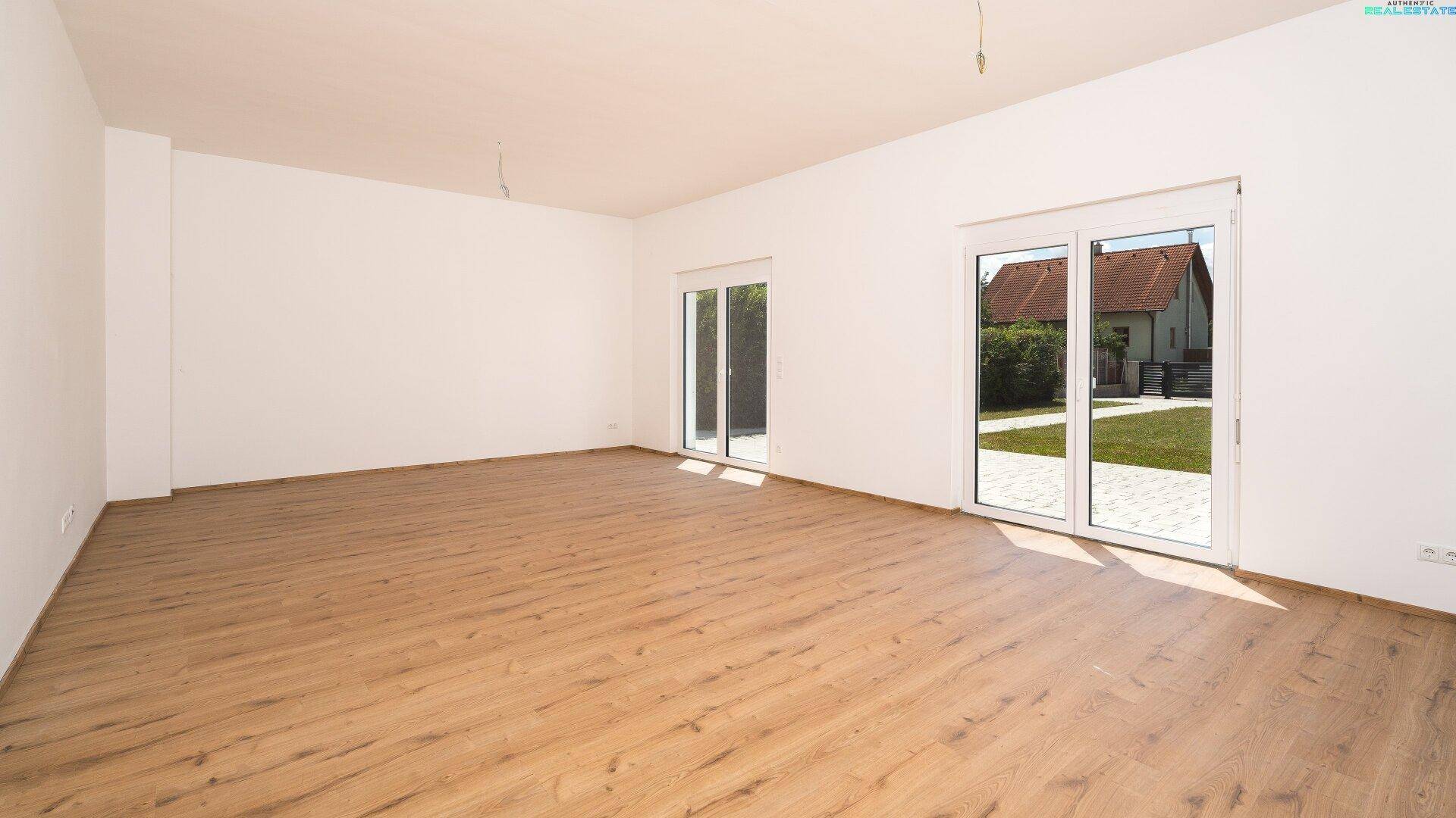 Geräumiger Wohnbereich mit Laminatboden und Zugang zum Garten durch große Fenster.