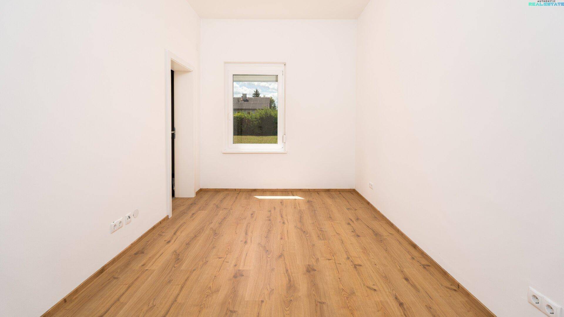 Helles Schlafzimmer mit Laminatboden und einem Fenster mit Blick ins Grüne.