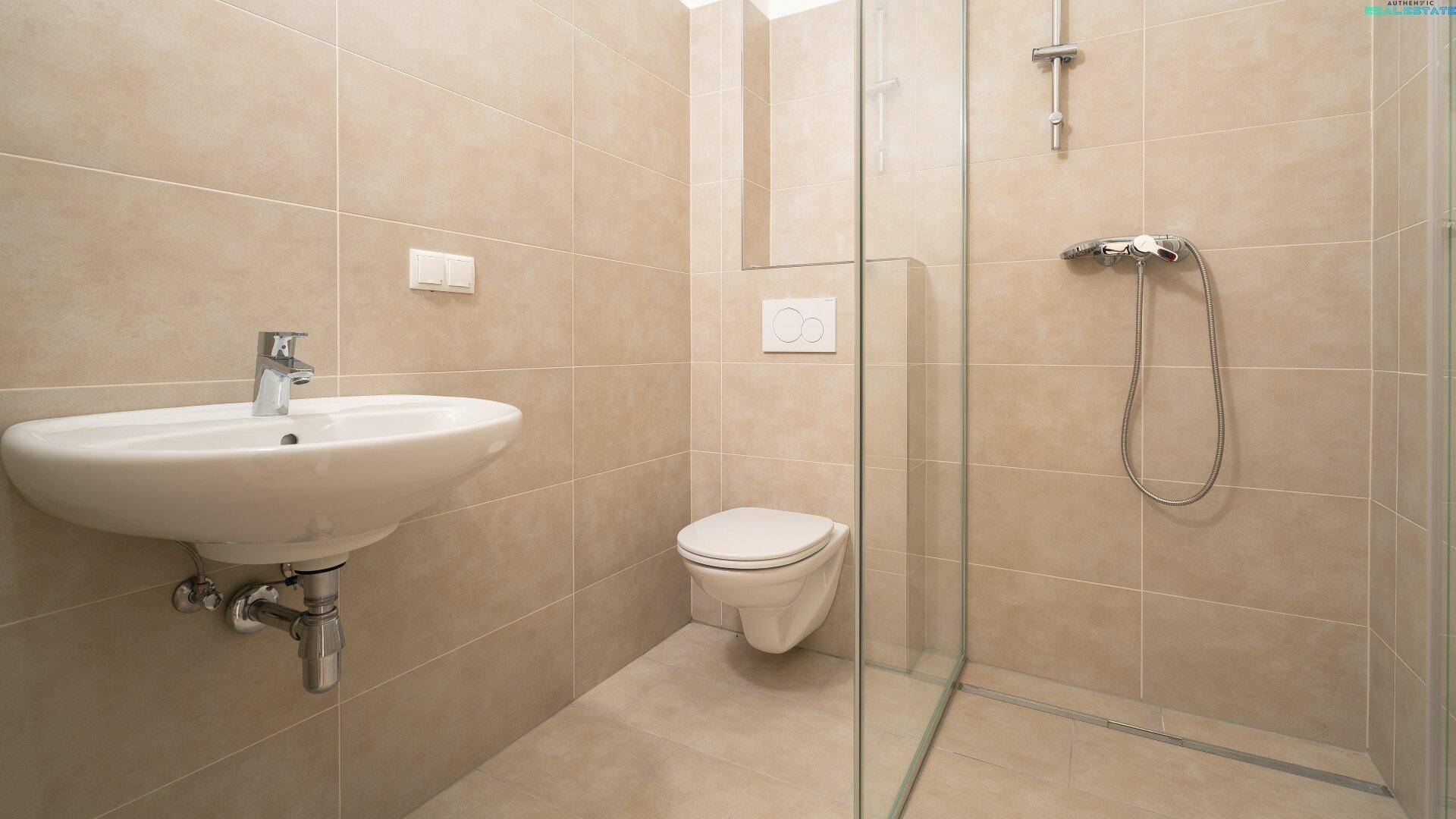 Modernes Badezimmer mit beigefarbenen Fliesen, Dusche und wandhängendem WC.
