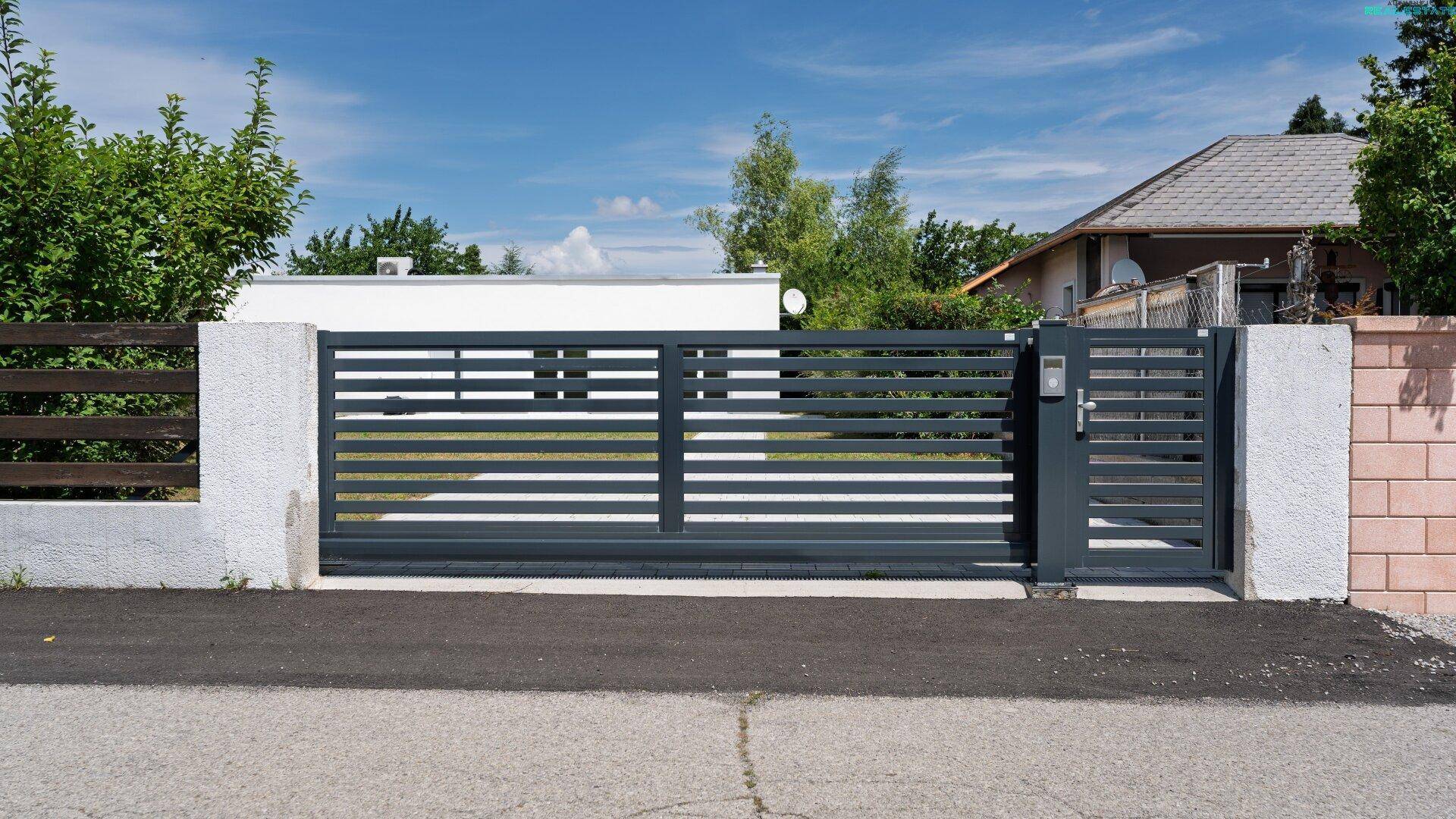 Modernes Einfahrtstor mit horizontalen Lamellen und Zugang zum Grundstück.