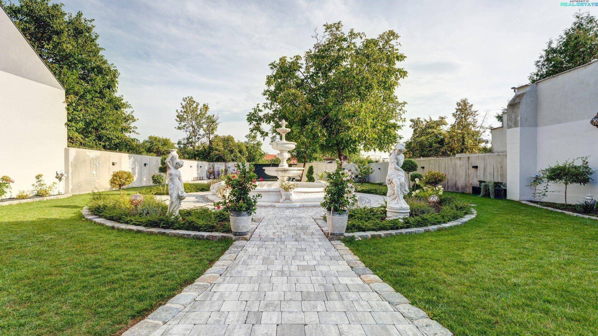 Weitläufiger Garten mit zentralem Springbrunnen, gepflegten Rasenflächen und dekorativen Statuen.