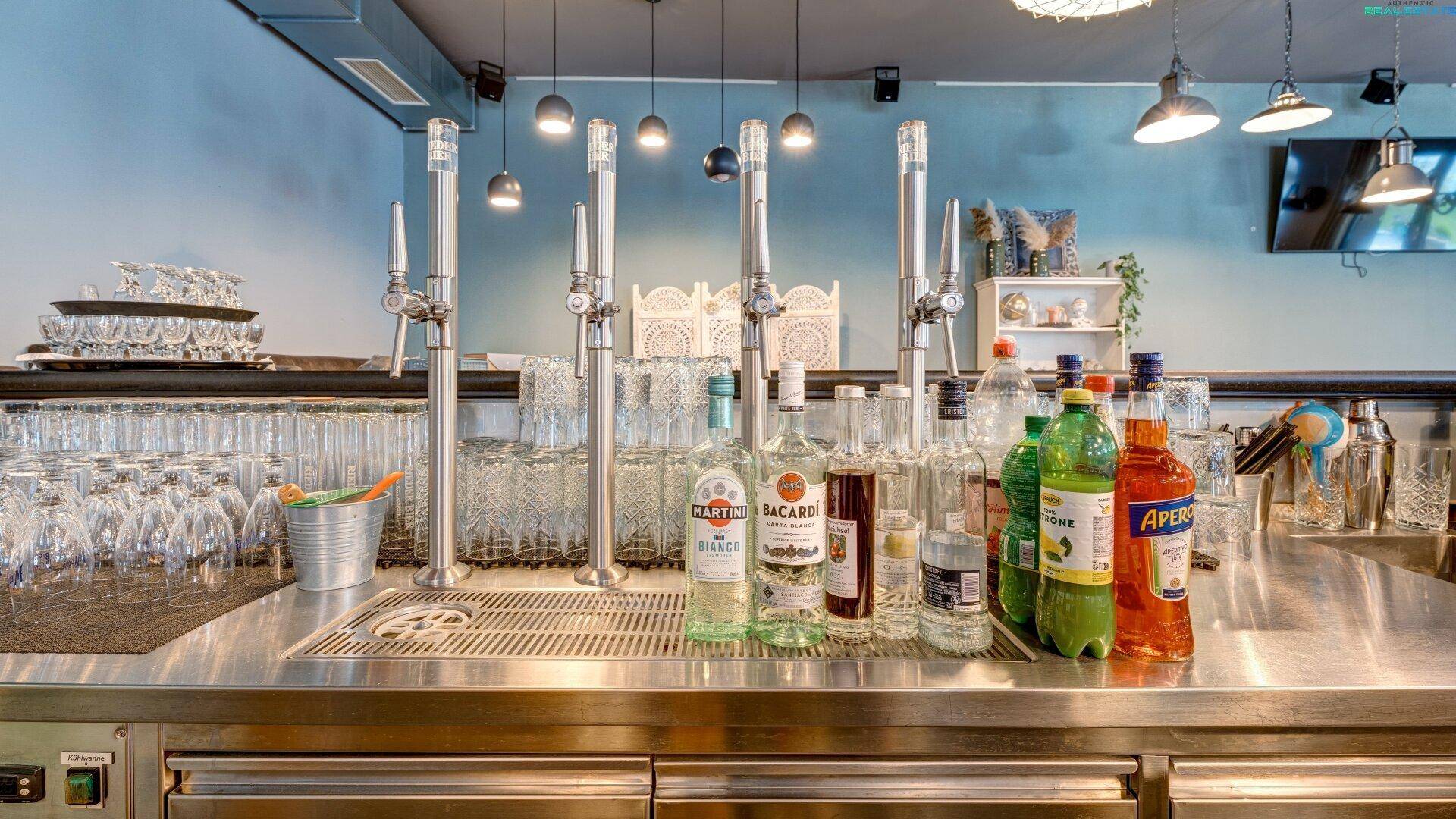Detailansicht einer Bar mit Zapfanlagen, verschiedenen Flaschen und gestapelten Gläsern.