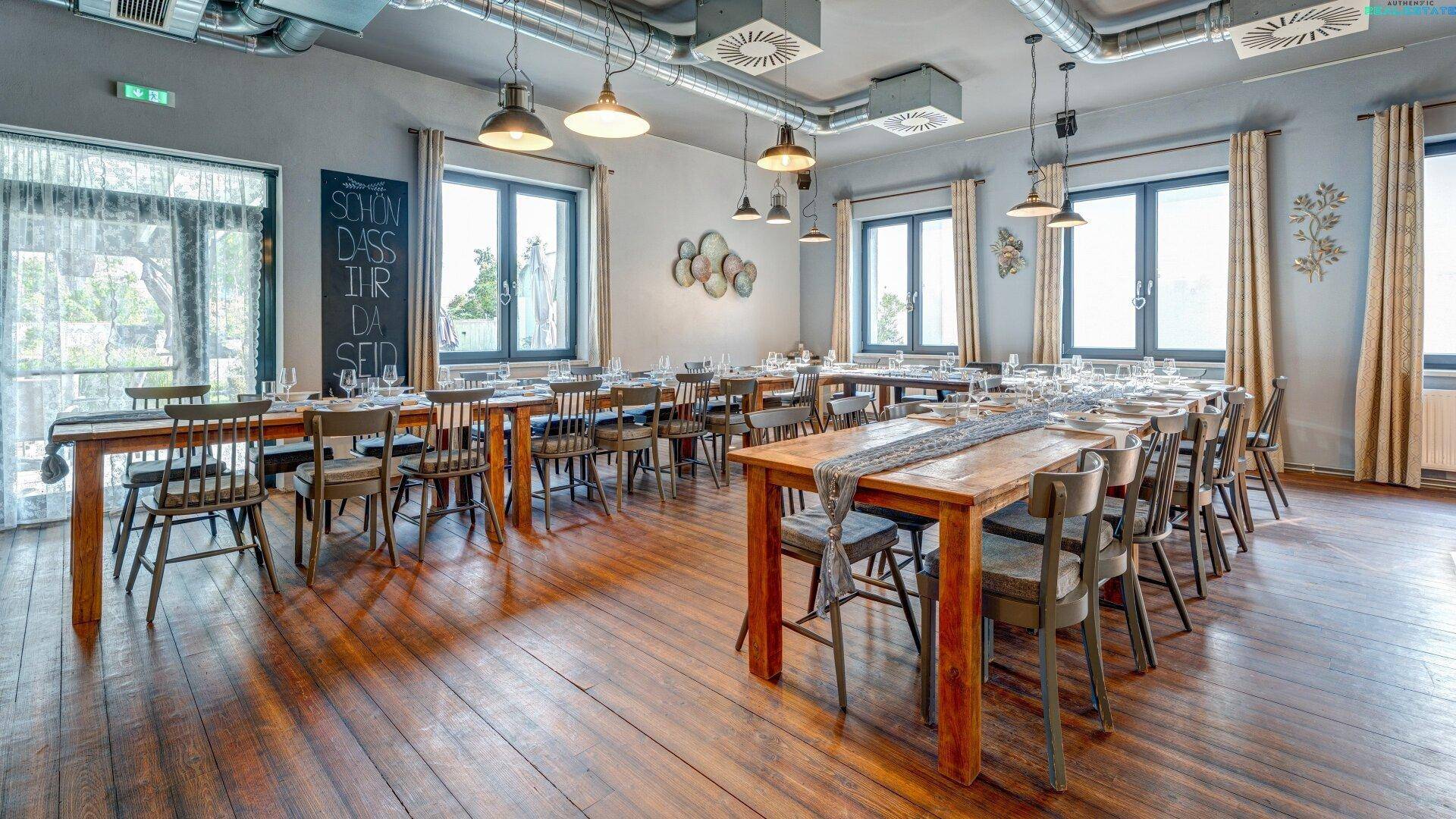 Großer Speisesaal mit Holztischen, Stühlen und sichtbaren Lüftungsrohren im industriellen Stil.