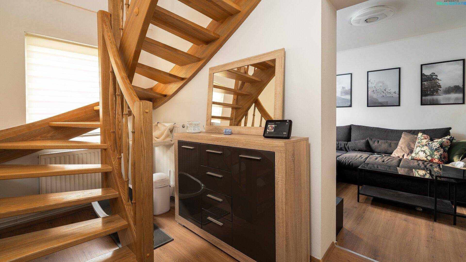 Heller Flur mit Holztreppe, Kommode und Spiegel, der zum Wohnbereich führt.