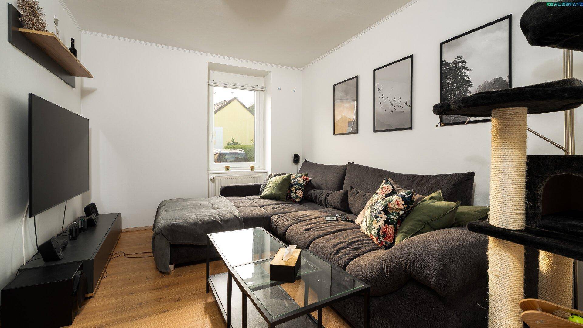 Helles Wohnzimmer mit großem Ecksofa, Fernseher und Blick ins Grüne.