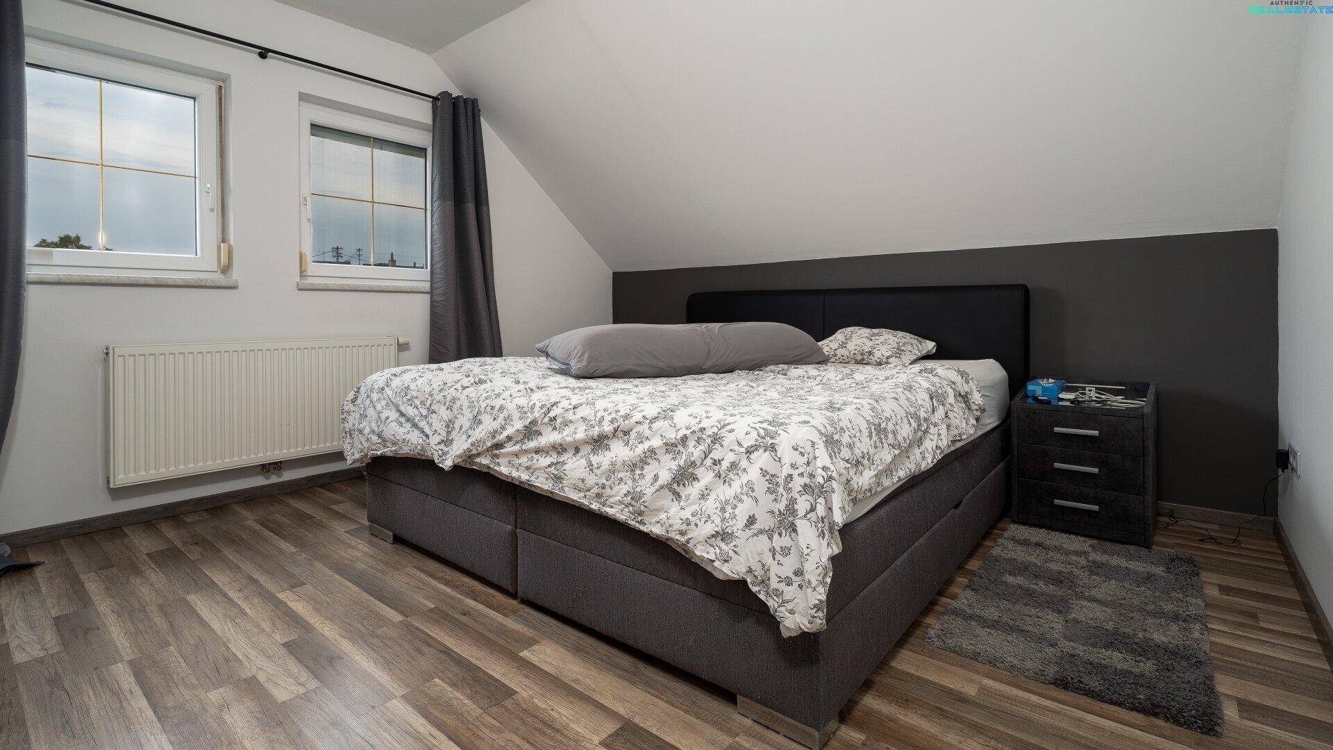 Schlafzimmer mit Doppelbett, Nachttisch und Dachschrägen, gut beleuchtet.
