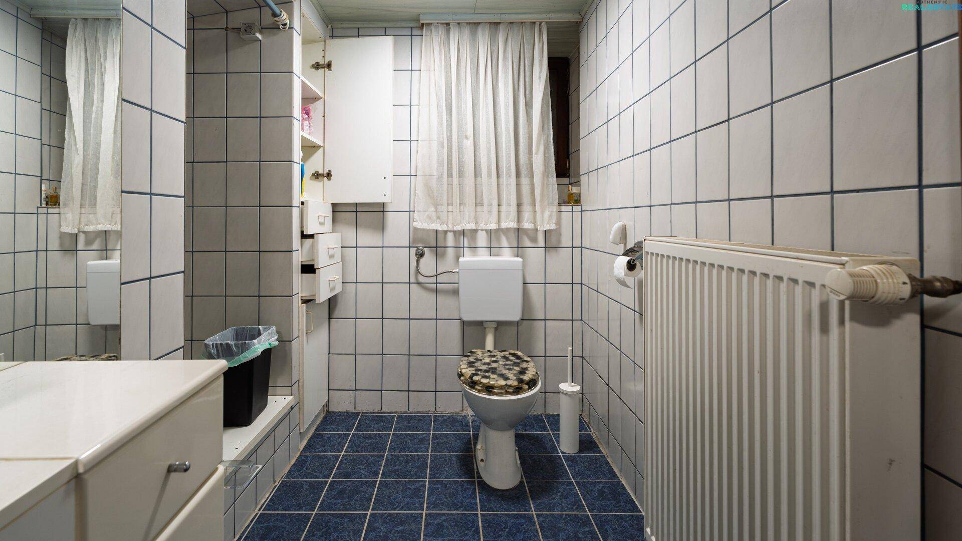 Kleines WC mit blauen Bodenfliesen, weißen Wandfliesen und Heizkörper.