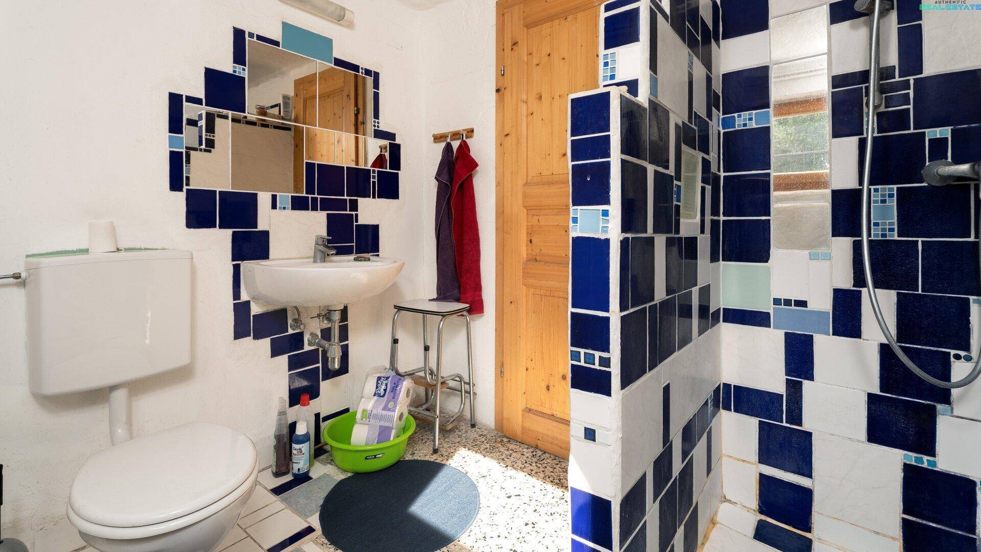 Badezimmer mit auffälligen blau-weißen Fliesen, Toilette, Waschbecken und Duschbereich.