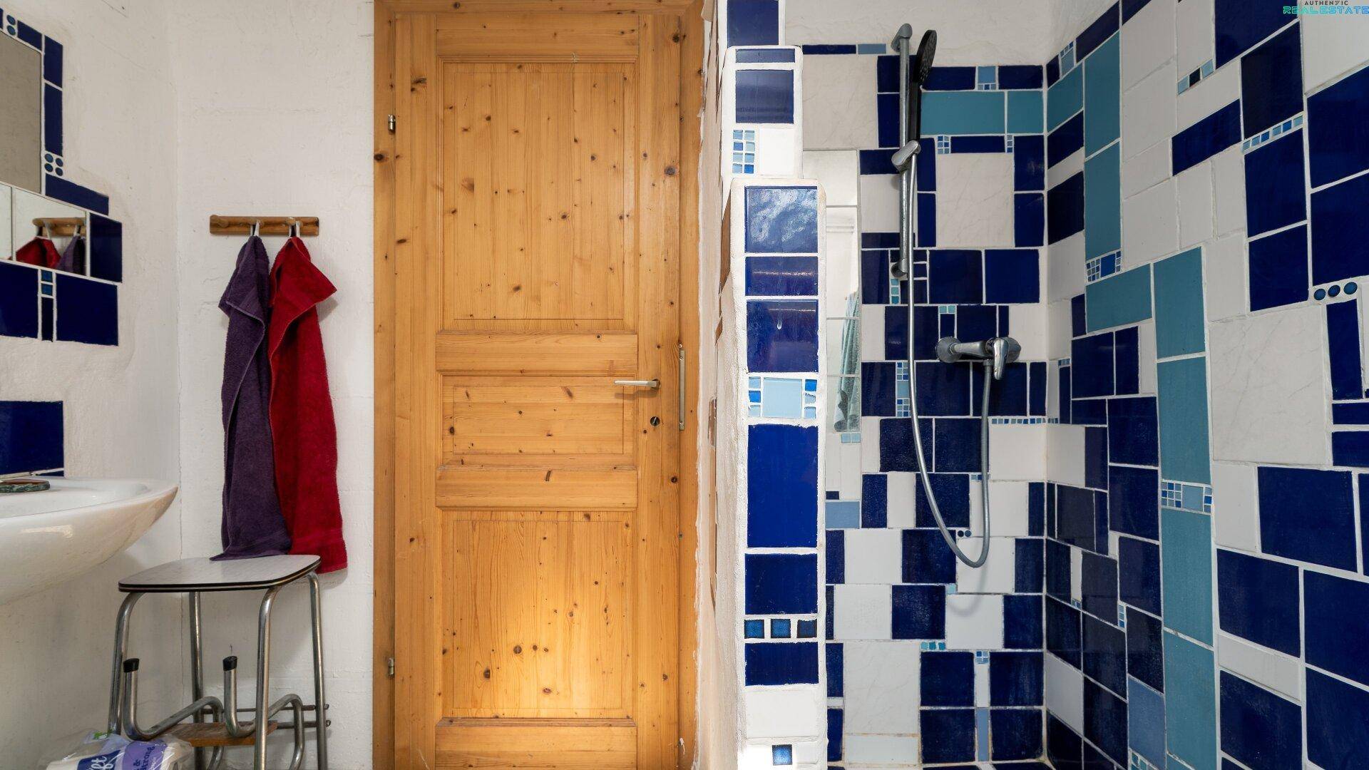 Holztür und Duschbereich mit blauen und weißen Fliesen im Badezimmer.