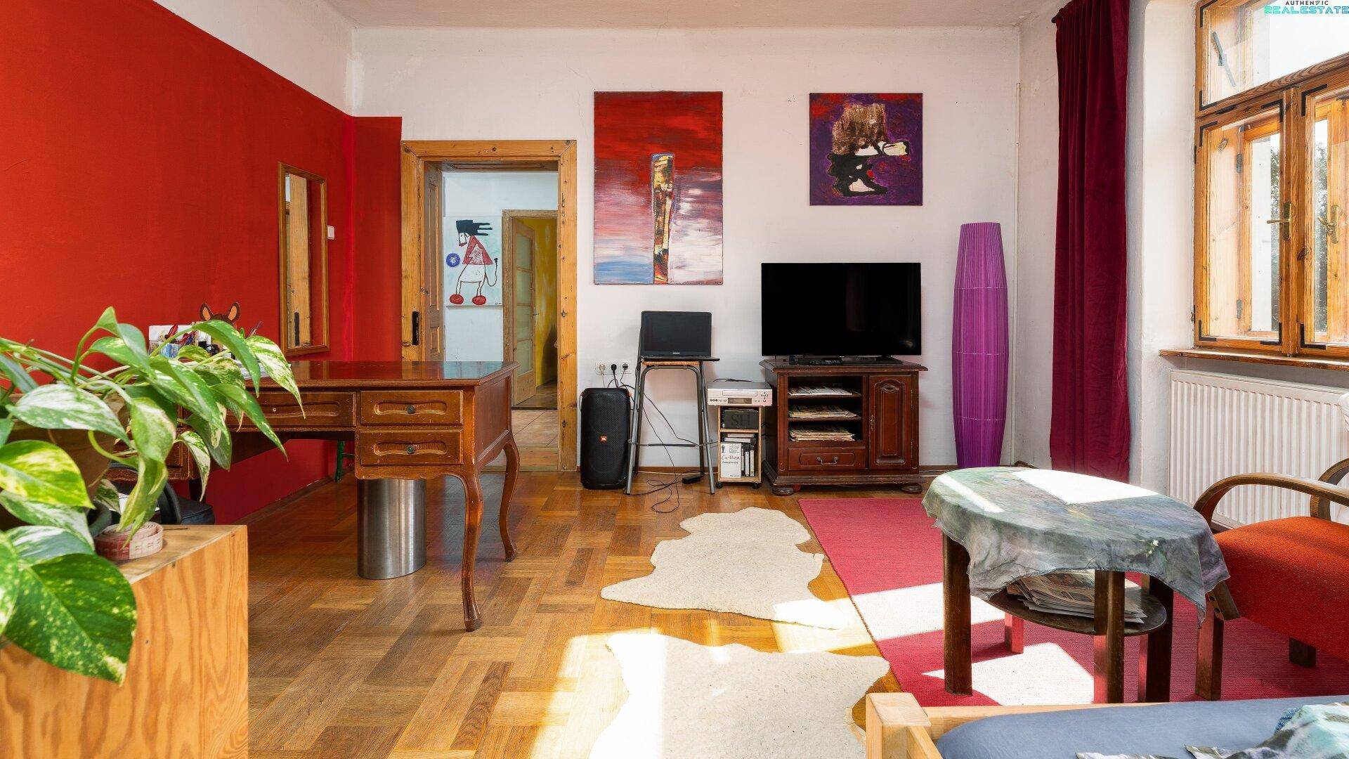 Wohnzimmer oder Arbeitsbereich mit Schreibtisch, Fernseher und roter Akzentwand.