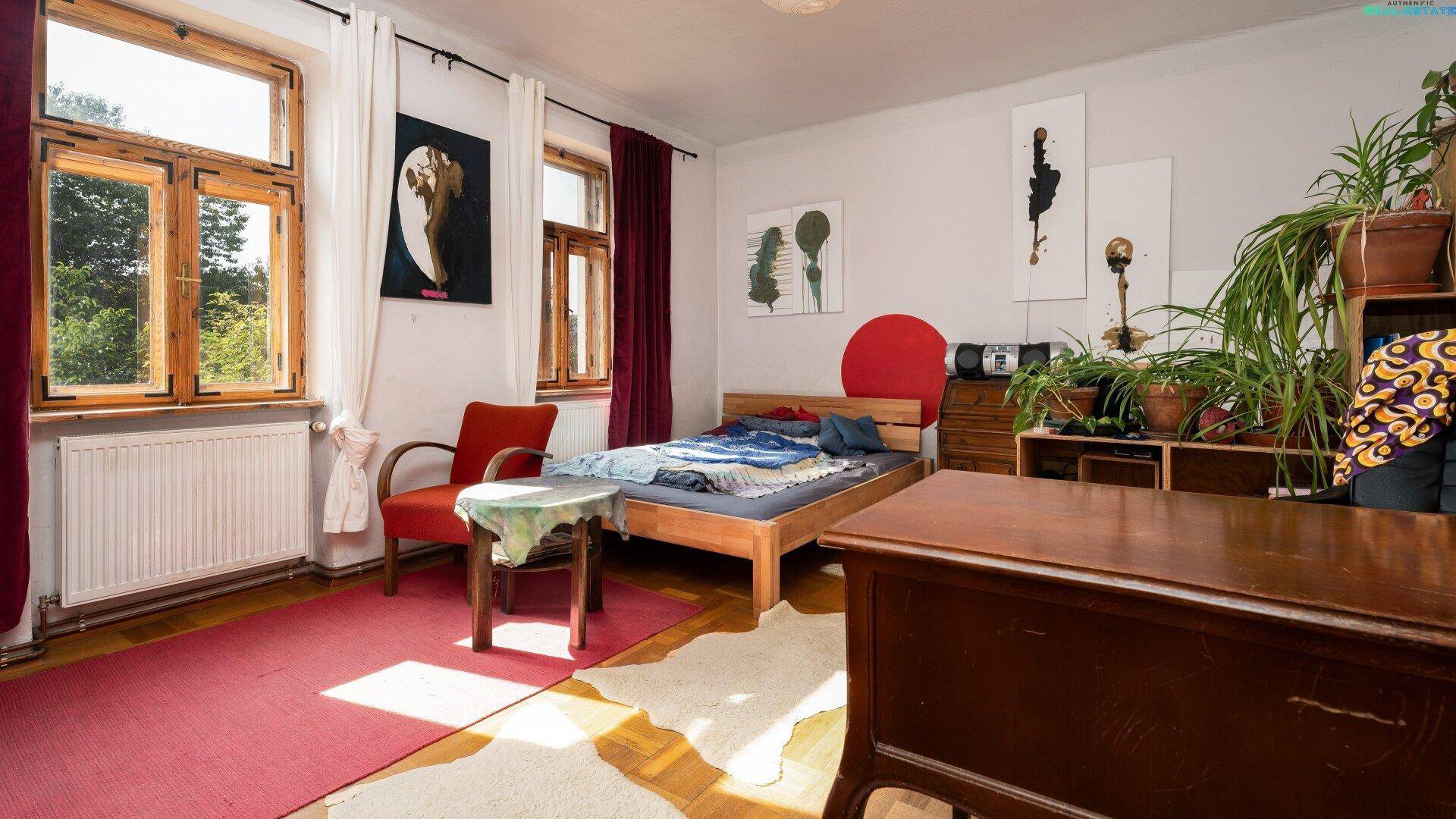 Schlafzimmer mit Bett, Holzboden, großen Fenstern und Pflanzen.