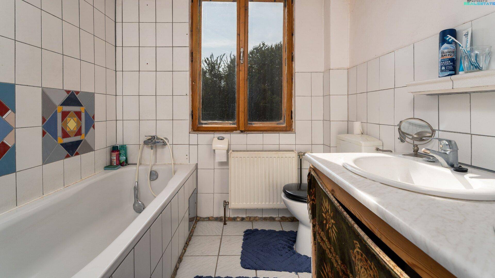 Badezimmer mit Badewanne, Toilette, Waschbecken und Fenster, hell gefliest.