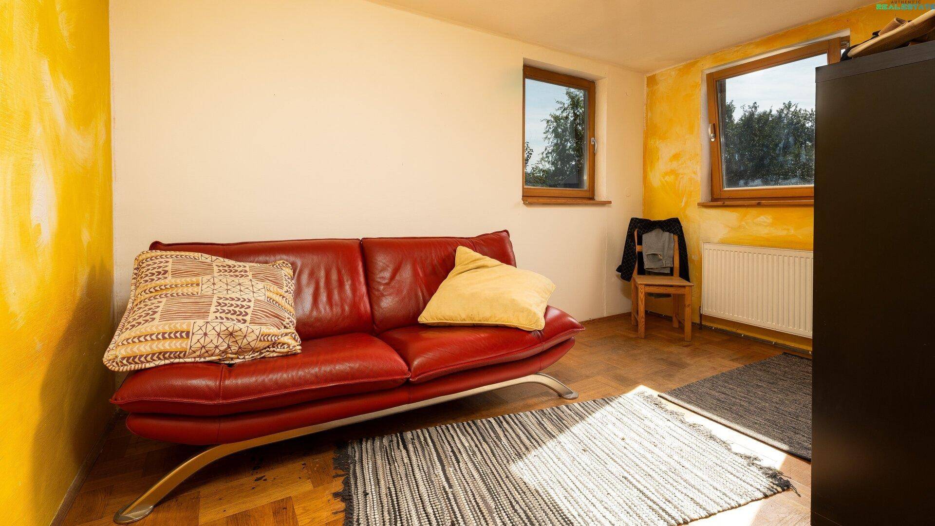 Gemütlicher Raum mit rotem Sofa, gelber Akzentwand und Holzboden.