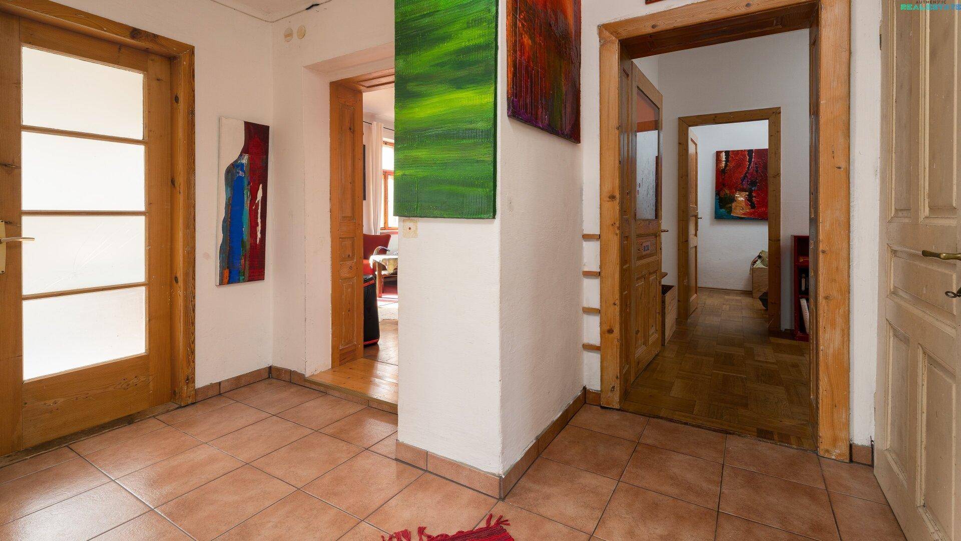 Flur mit gefliestem Boden und mehreren Holztüren, dekoriert mit Kunstwerken.