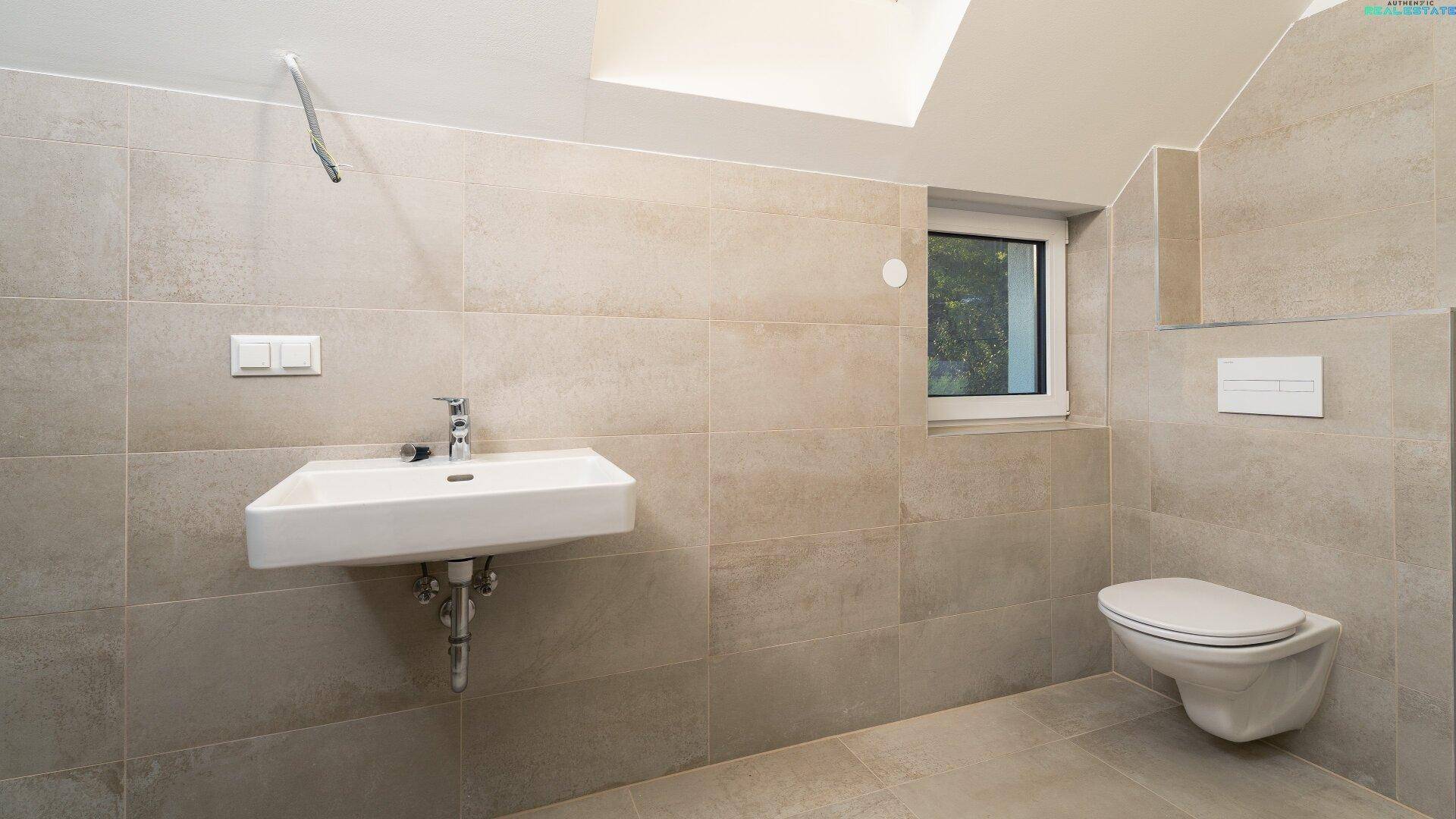 Helles Badezimmer mit Waschbecken, WC, Fenster und modernen Fliesen, einladend und gepflegt.