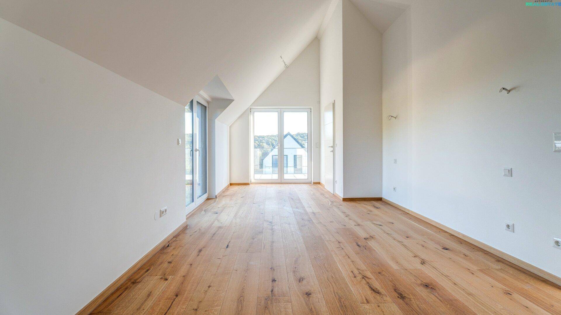 Helles Dachgeschosszimmer mit Holzboden, hohen Decken und großen Fenstern, die viel Licht hereinlassen.