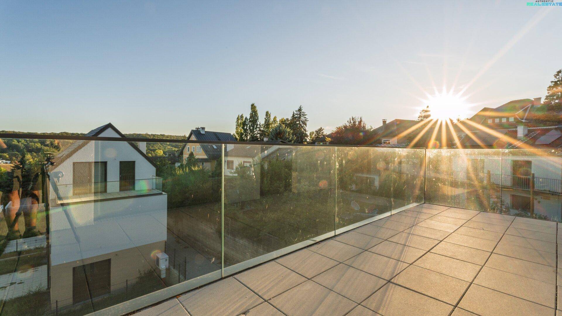 Geräumige Terrasse mit Glasgeländer und weitem Blick über die Landschaft bei Sonnenuntergang.