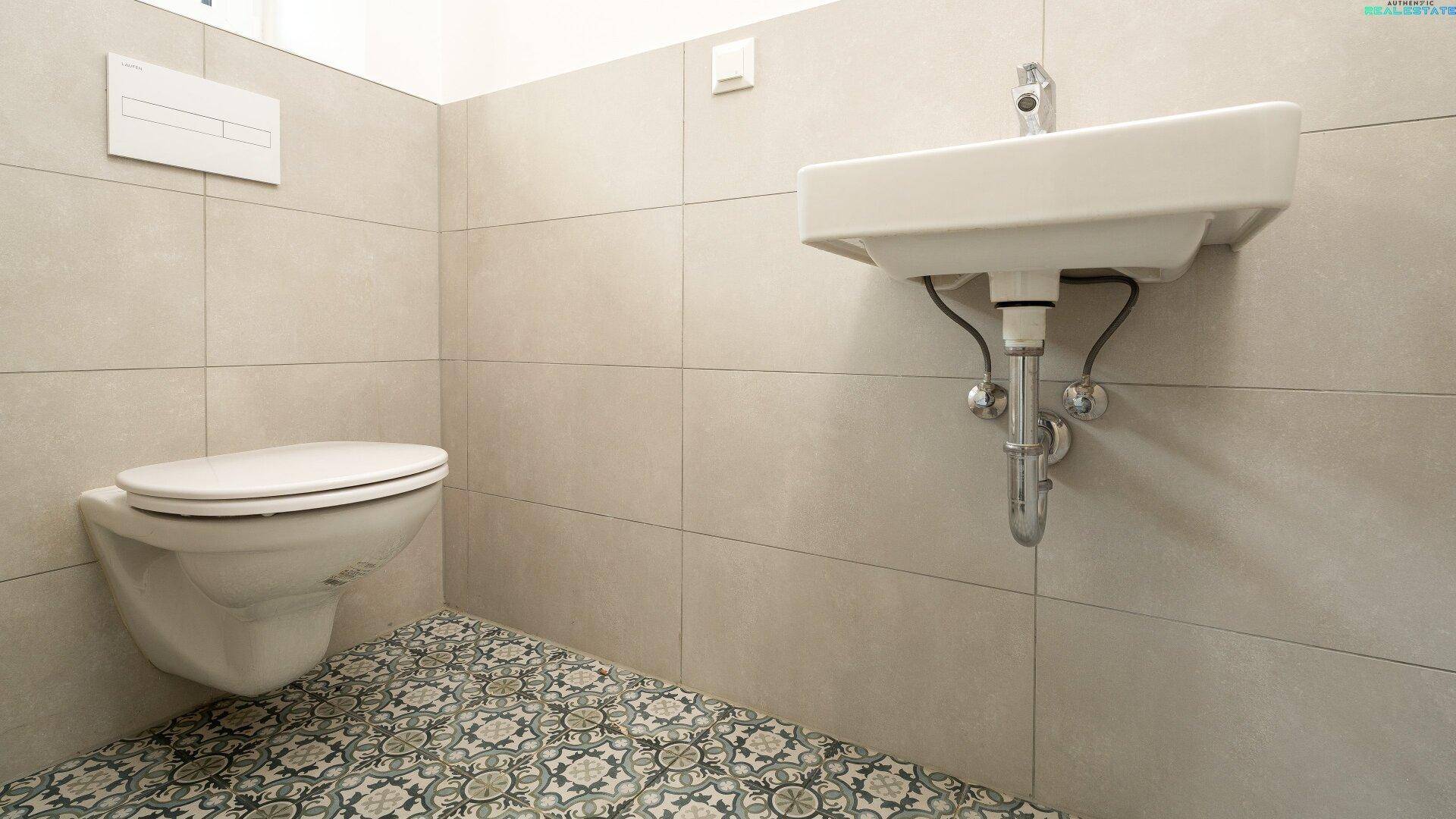 Modernes Gäste-WC mit Wand-WC, Waschbecken und gemusterten Bodenfliesen in zeitgemäßem Design.